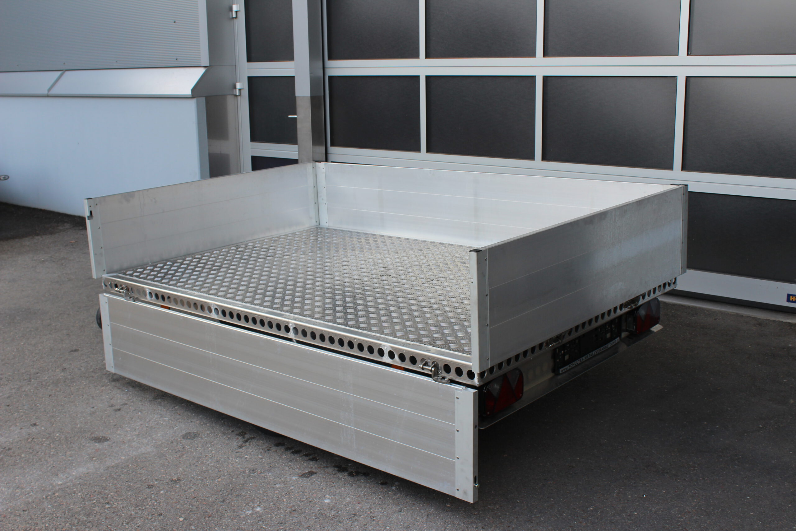 Aluminium Plattformanhänger mit Aluminium Bordwänden vor einem Hallentor