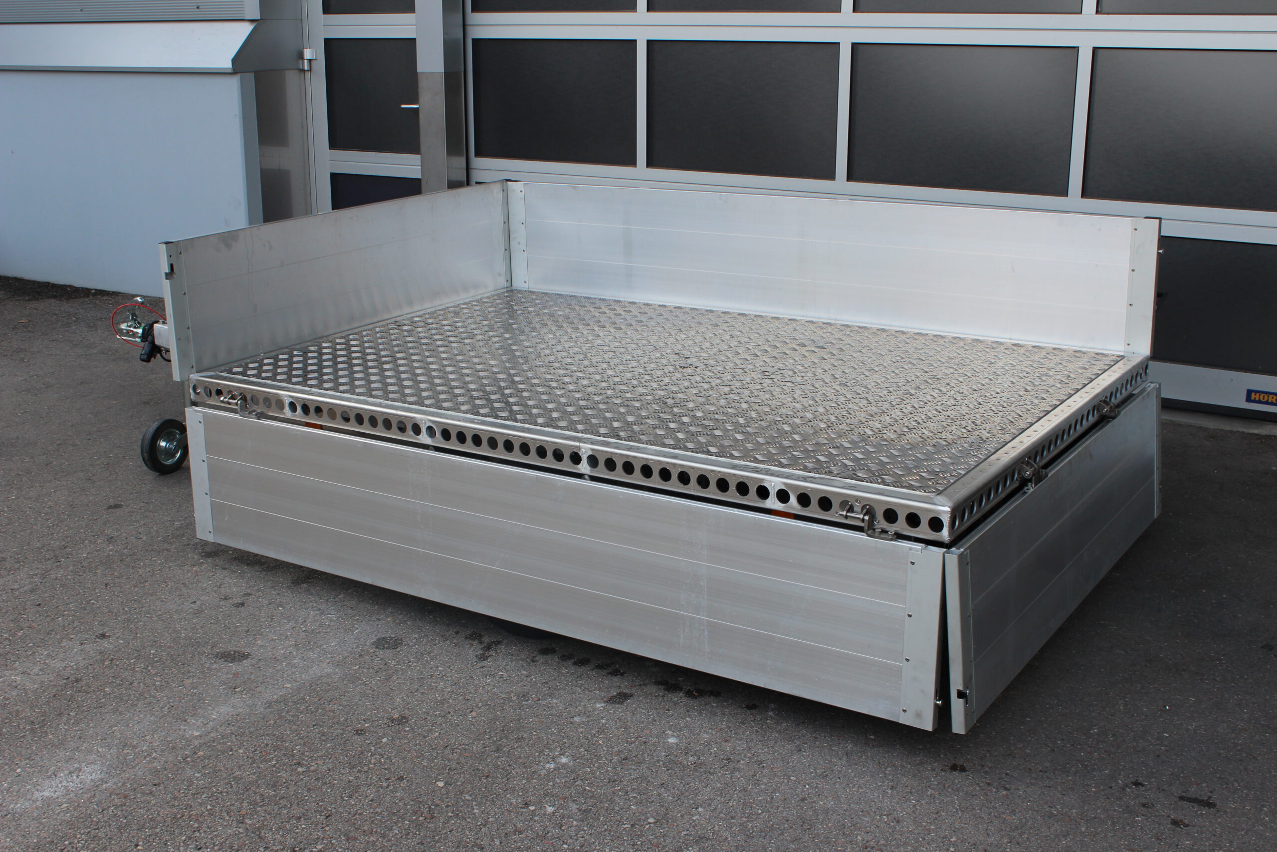 Aluminium Plattformanhänger mit Aluminium Bordwänden vor einem Hallentor