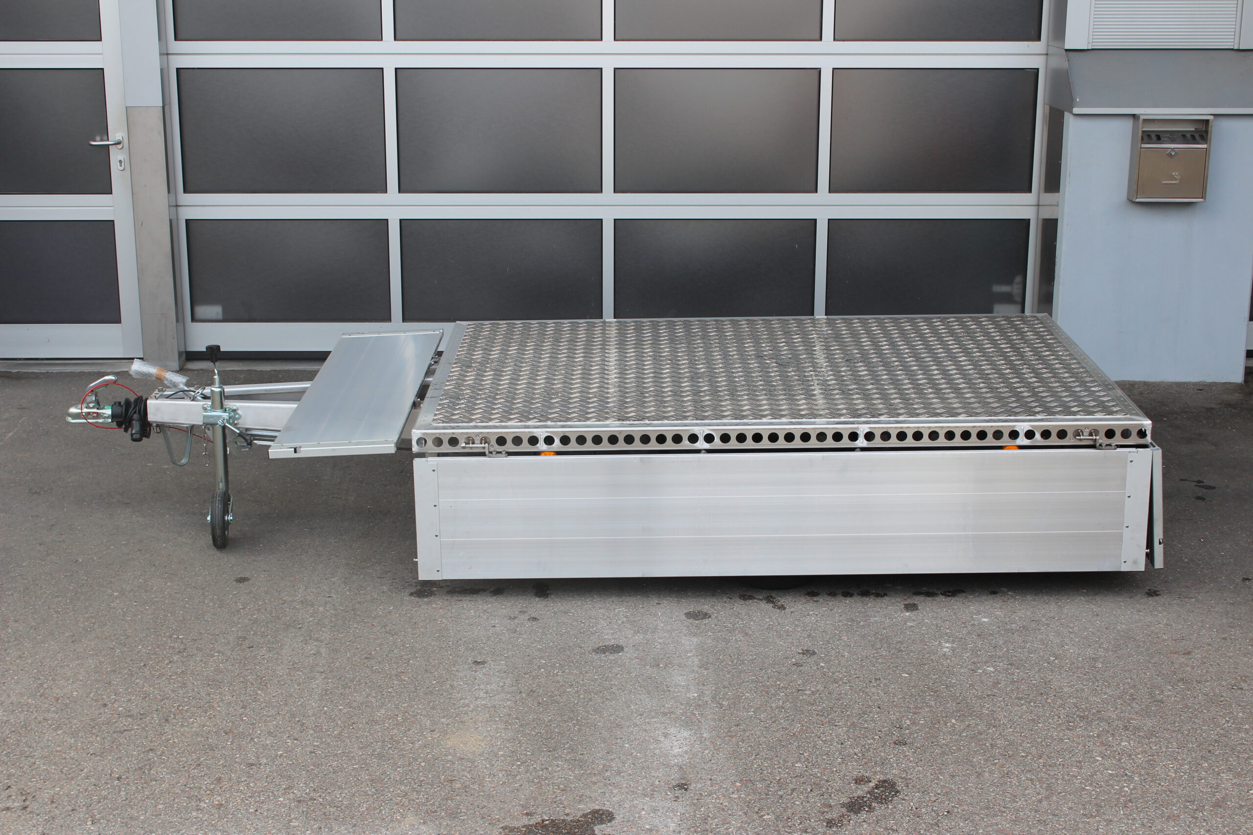 Aluminium Plattformanhänger mit Aluminium Bordwänden vor einem Hallentor