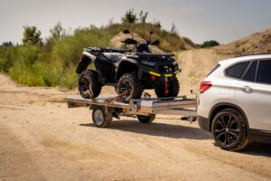Anhänger mit einem Quad hinter einem weißen Auto in einer Kiesgrube