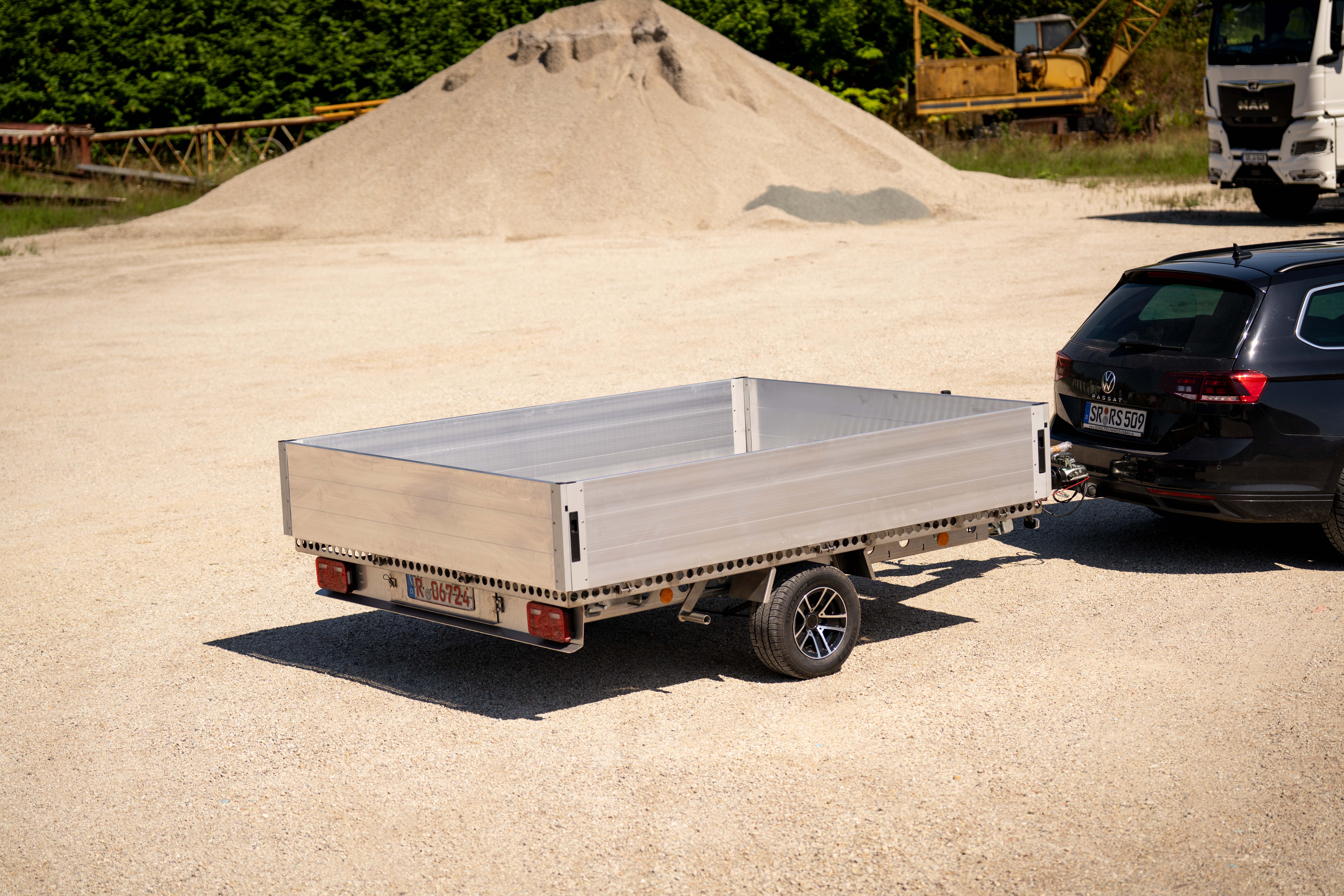 UA250 Plattformanhänger Alu mit Bordwänden Silberner Anhänger mit Bordwänden vor einem Sandhaufen