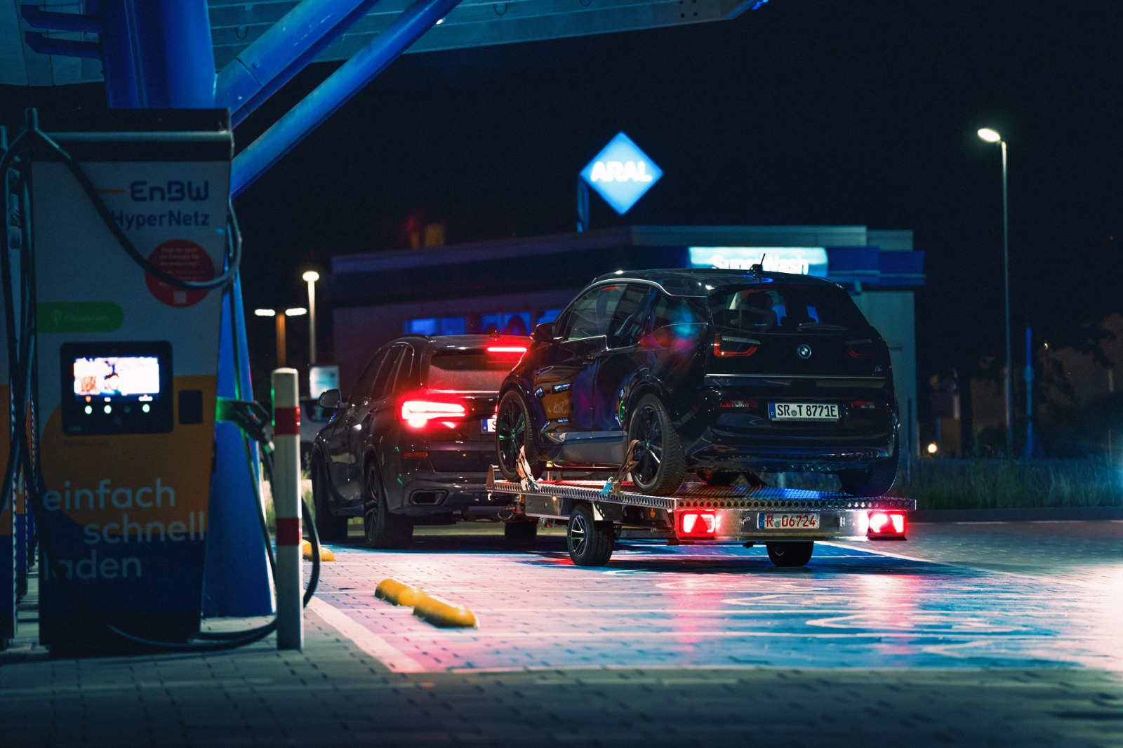 Auto-Anhänger mit einem BMW I3 beladen an einer Elektro-Ladestation