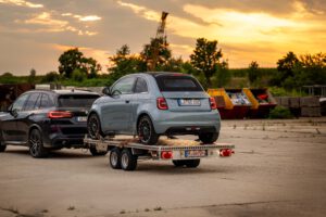 Anhänger aus Aluminium mit FIAT500 hinter einem BMW X5 vor auf einem Industriegelände mit Sonnenuntergang