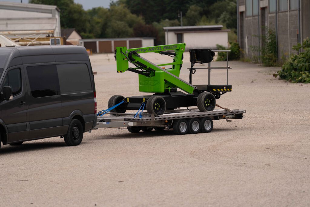 Anhänger aus Edelstahl mit einer grünen NIFTY Hebebühne auf einer Kiesfläche