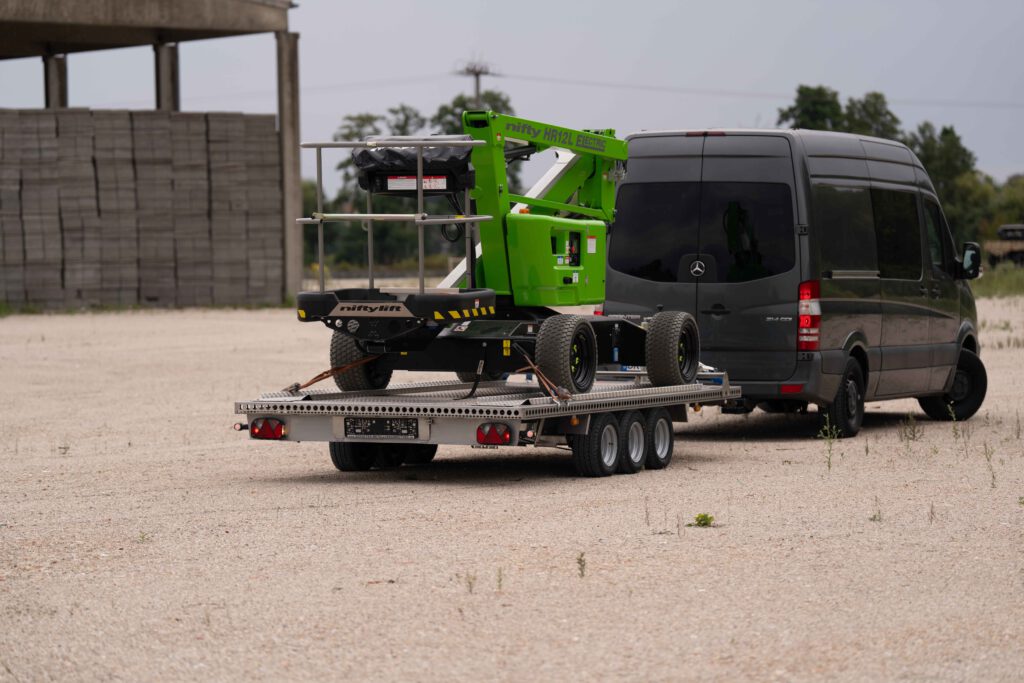Anhänger aus Edelstahl mit einer grünen NIFTY Hebebühne auf einer Kiesfläche