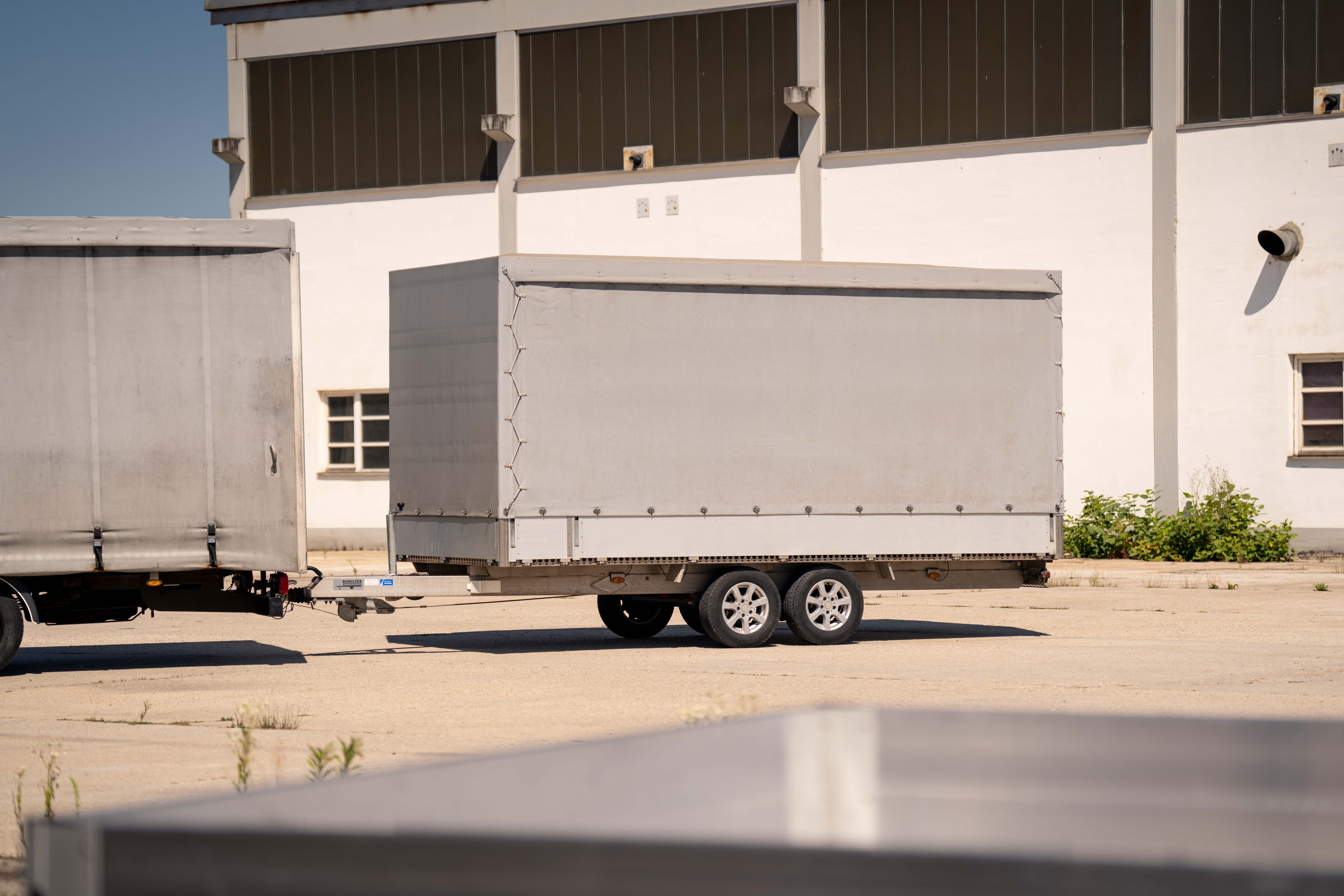 UA600 Planenaufbau Anhänger Grauer Planenanhänger vor einem Industriegebäude