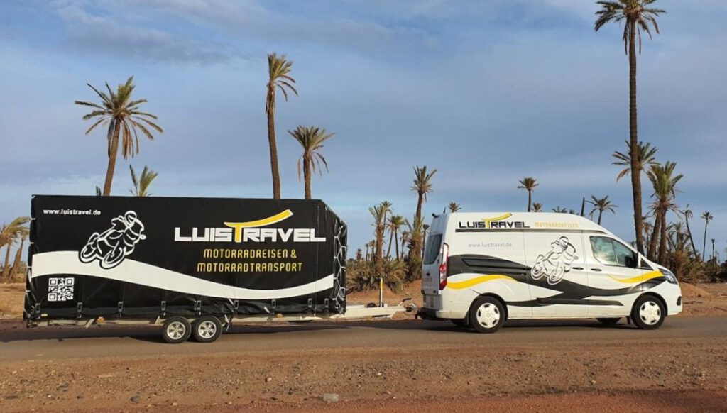 Ford Transit mit schwarzem Planenanhänger für Motorräder in einer Wüste unter Plamen