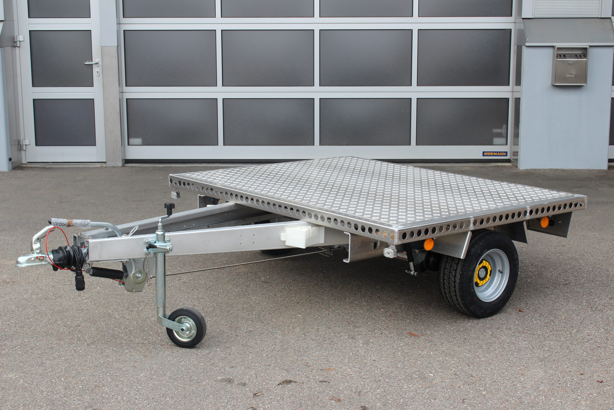 Kleiner Aluminium Plattformanhänger in silber vor einem grauen Hallentor