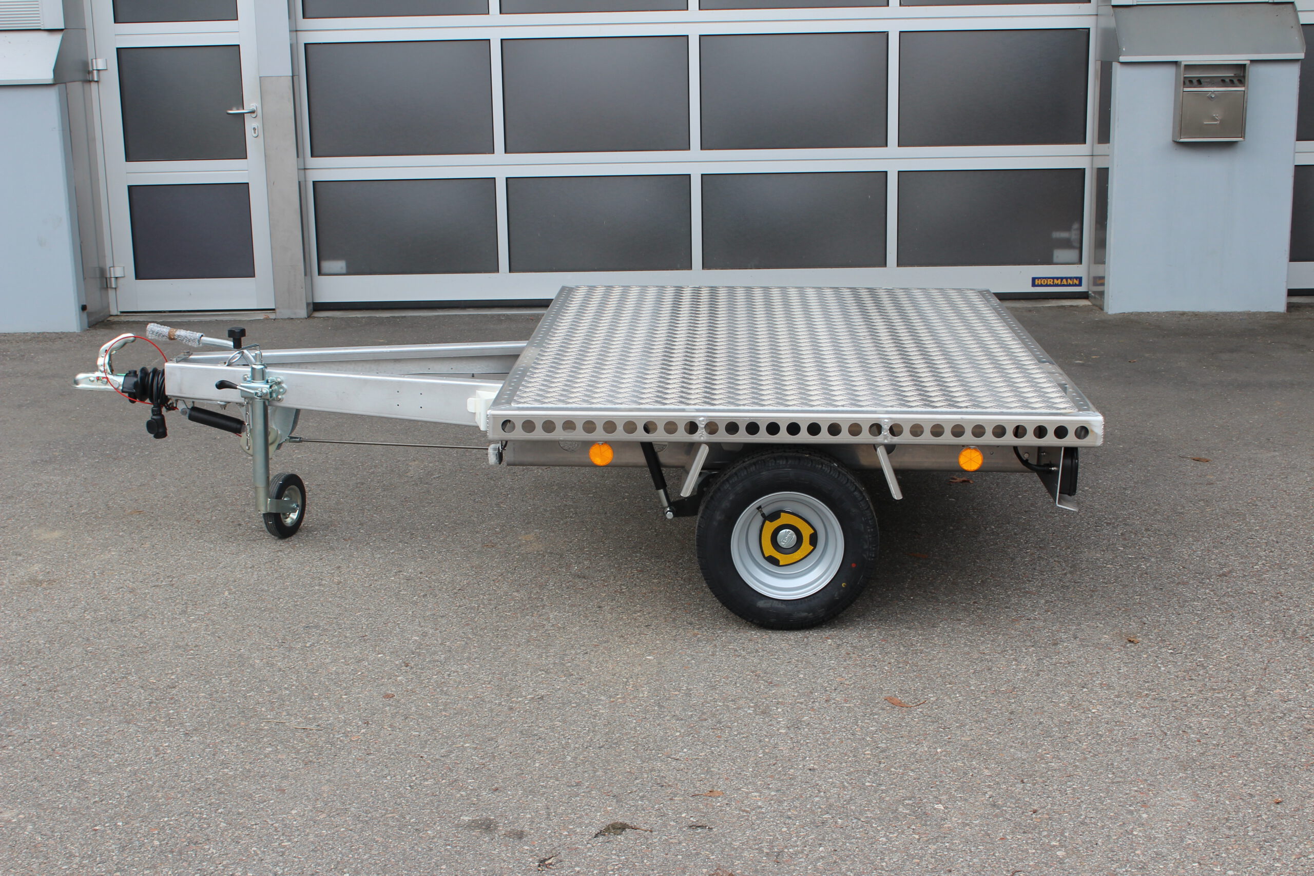 Kleiner Aluminium Plattformanhänger in silber vor einem grauen Hallentor