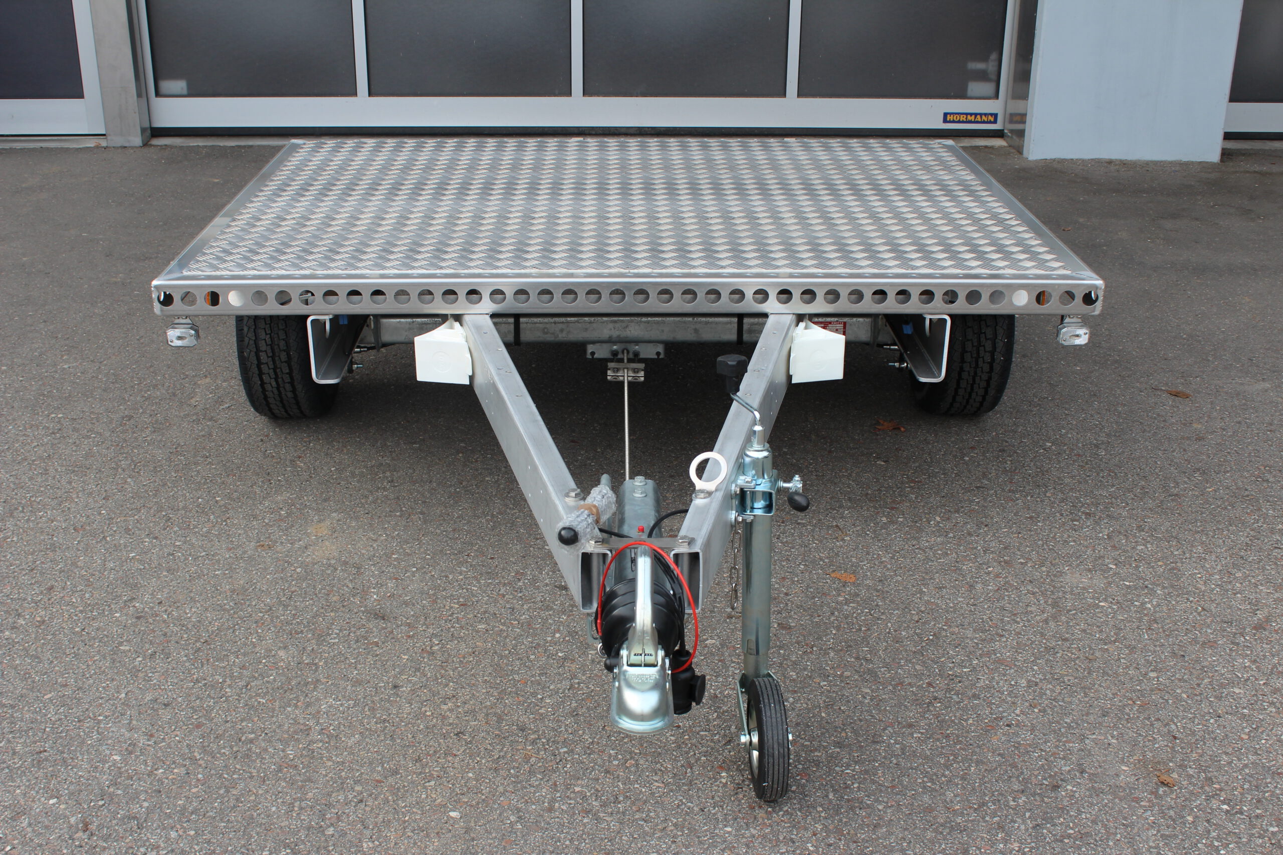 Kleiner Aluminium Plattformanhänger in silber vor einem grauen Hallentor