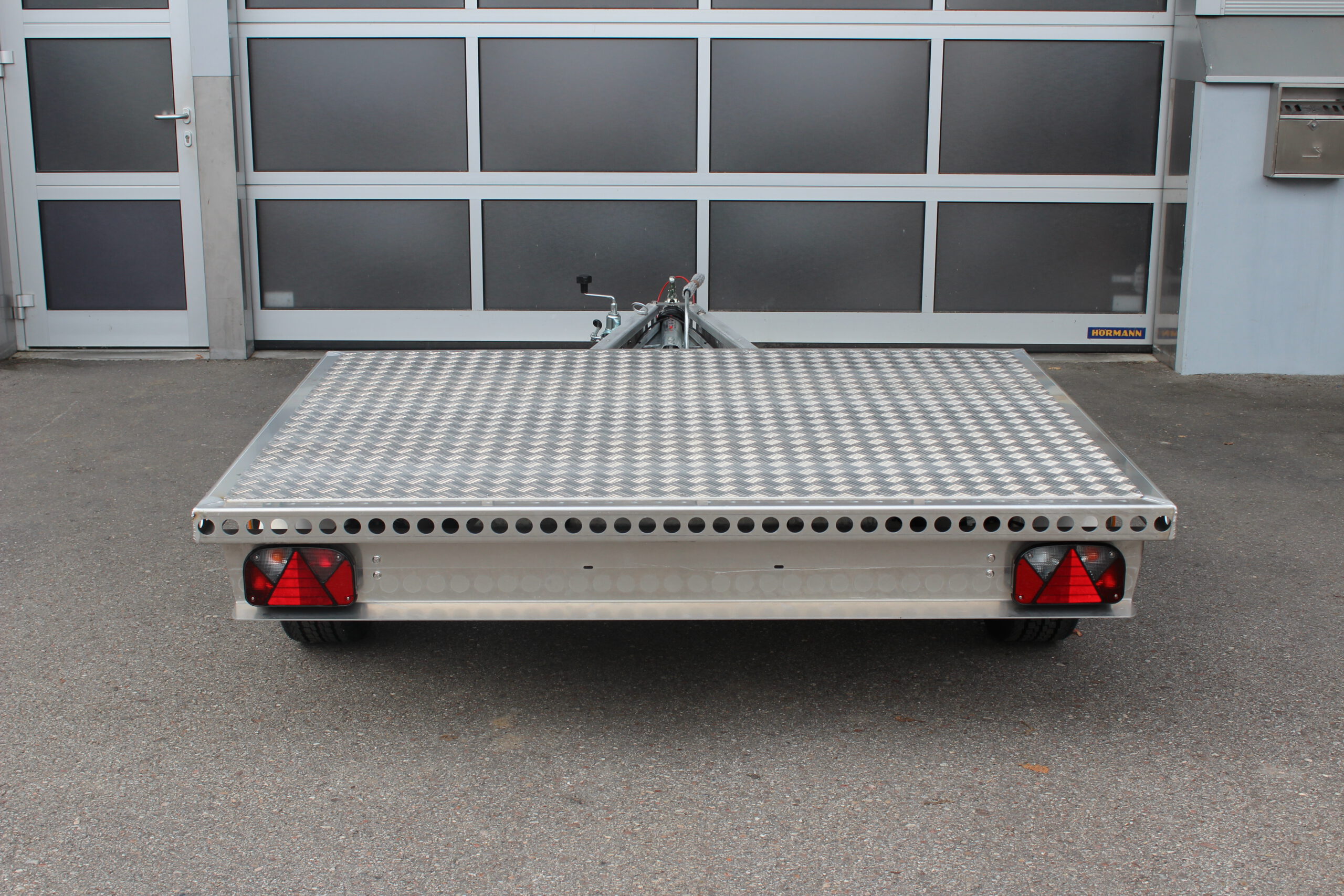 Kleiner Aluminium Plattformanhänger in silber vor einem grauen Hallentor