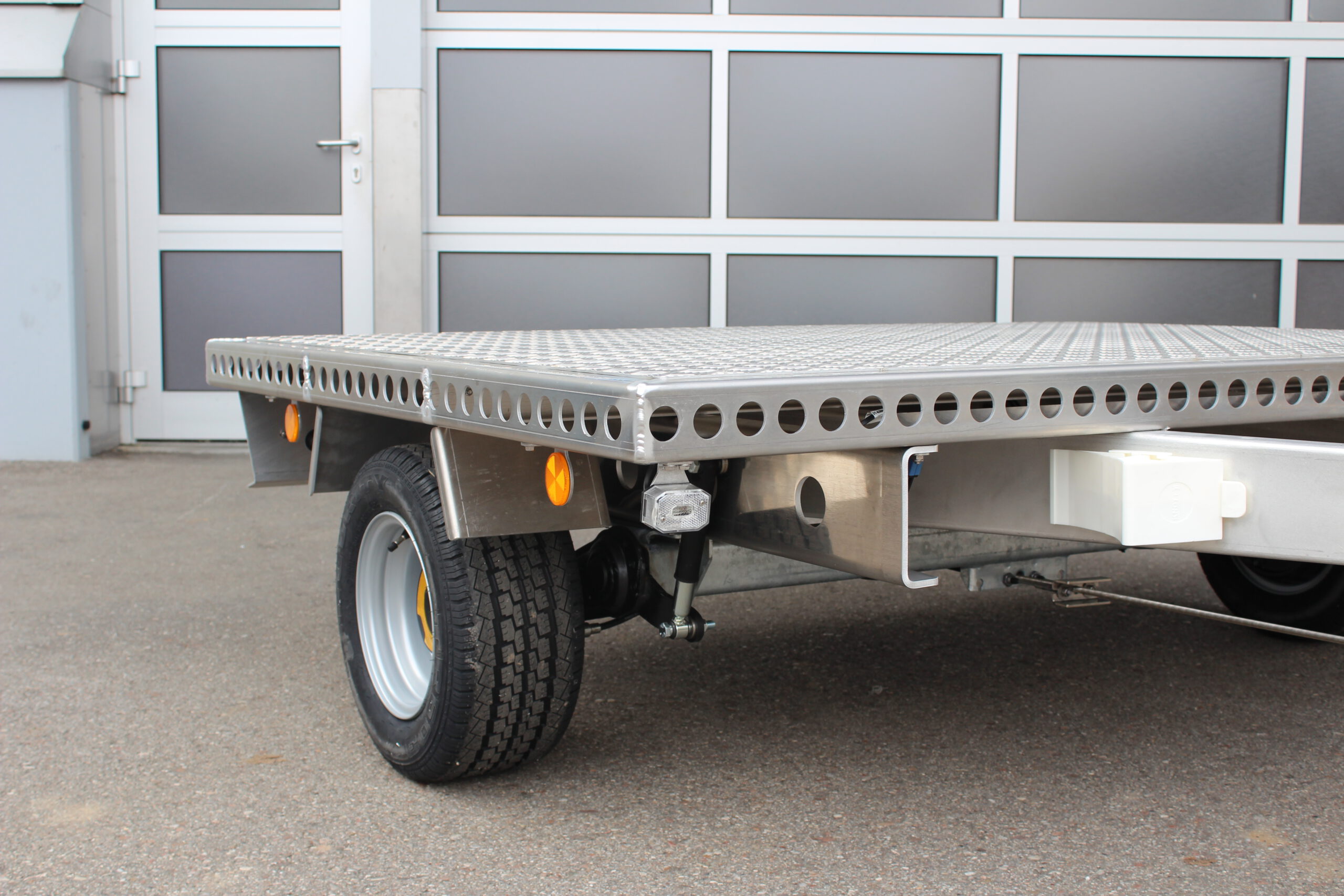 Kleiner Aluminium Plattformanhänger in silber vor einem grauen Hallentor