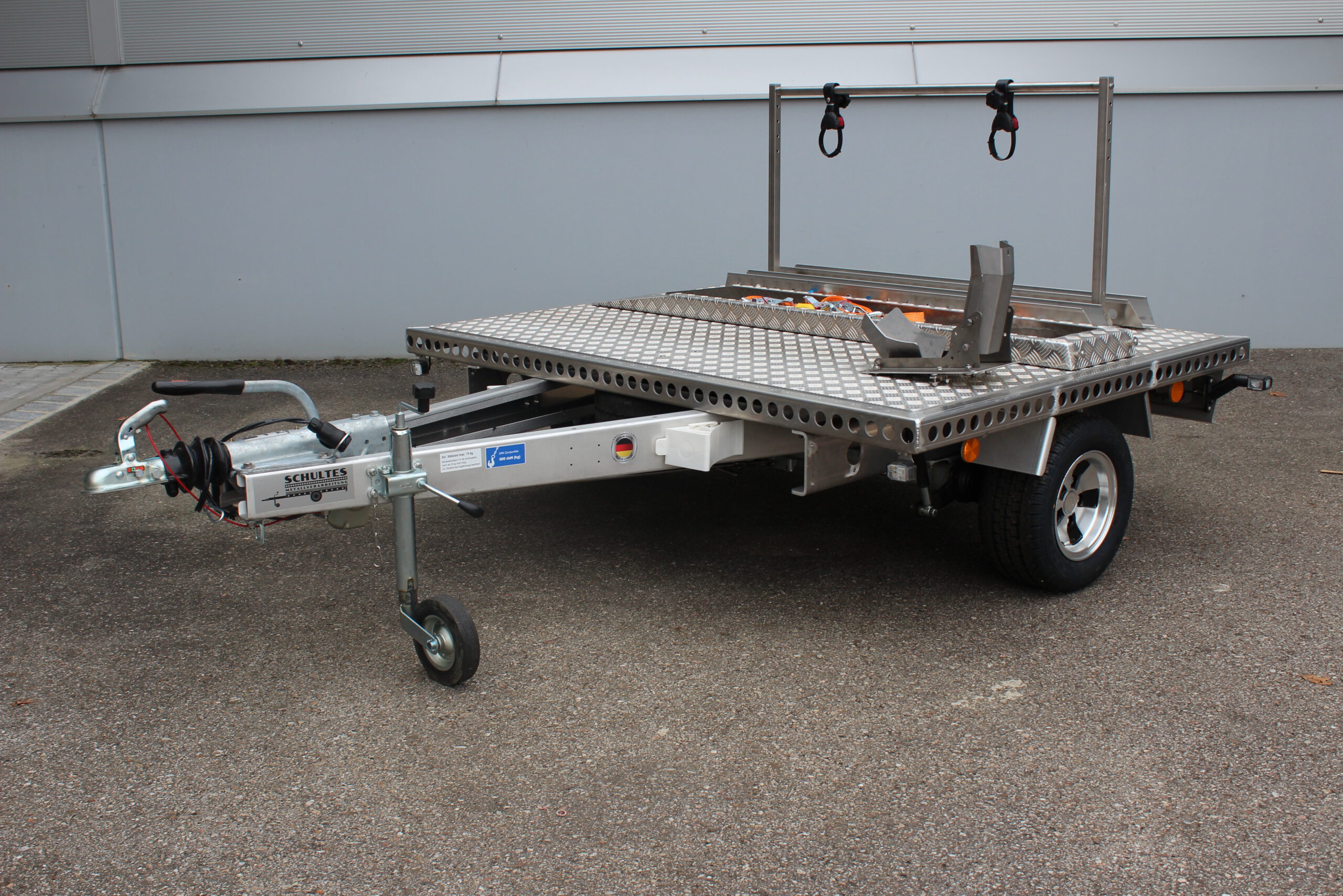 Aluminium Plattformanhänger mit Fahrradträger, Auffahrrampe und Radwippe vor einer grauen Wand