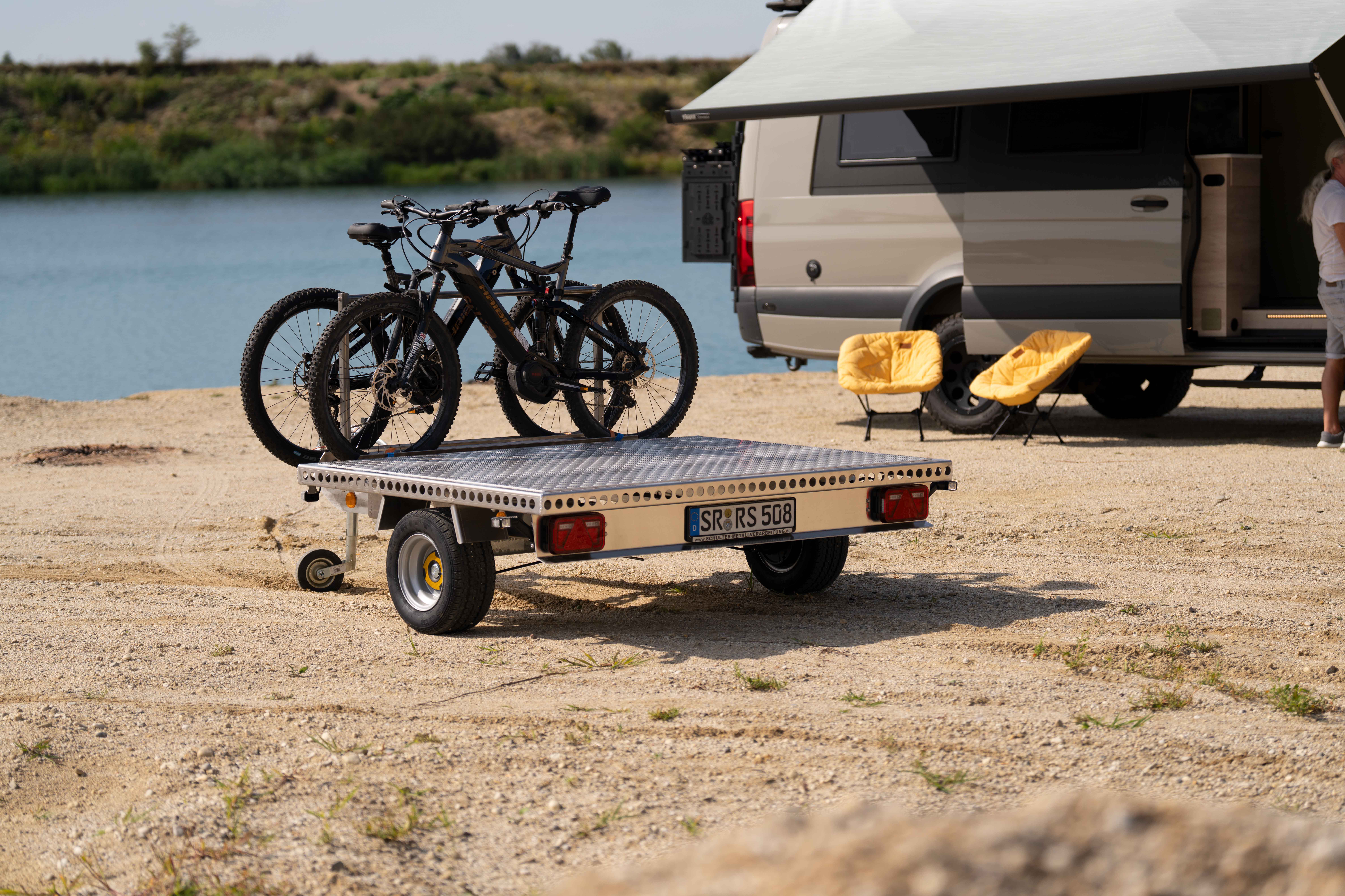 Aluminium Plattformanhänger mit zwei E-Bikes auf einer Sandfläche vor einem See