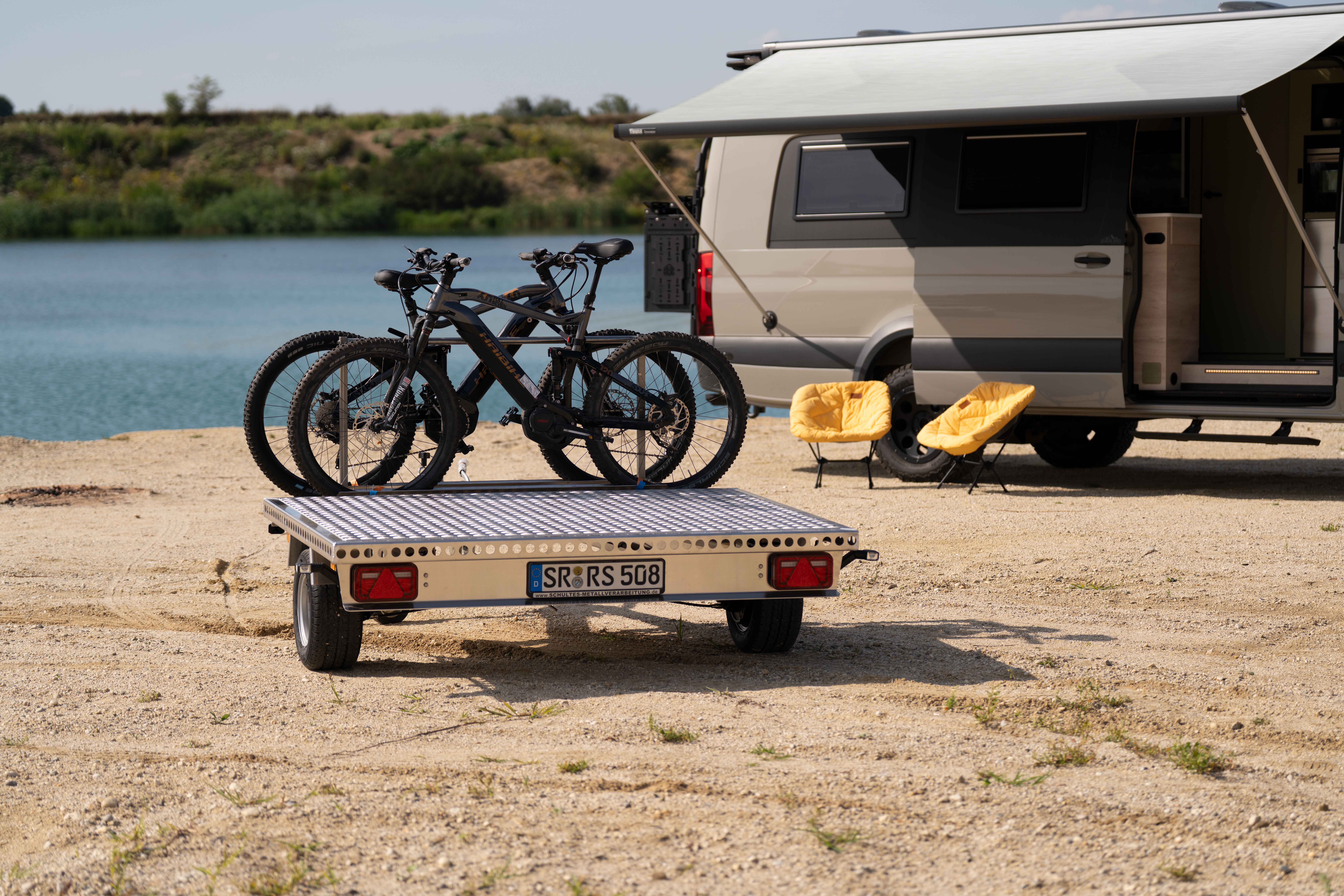 Aluminium Plattformanhänger mit zwei E-Bikes auf einer Sandfläche vor einem See