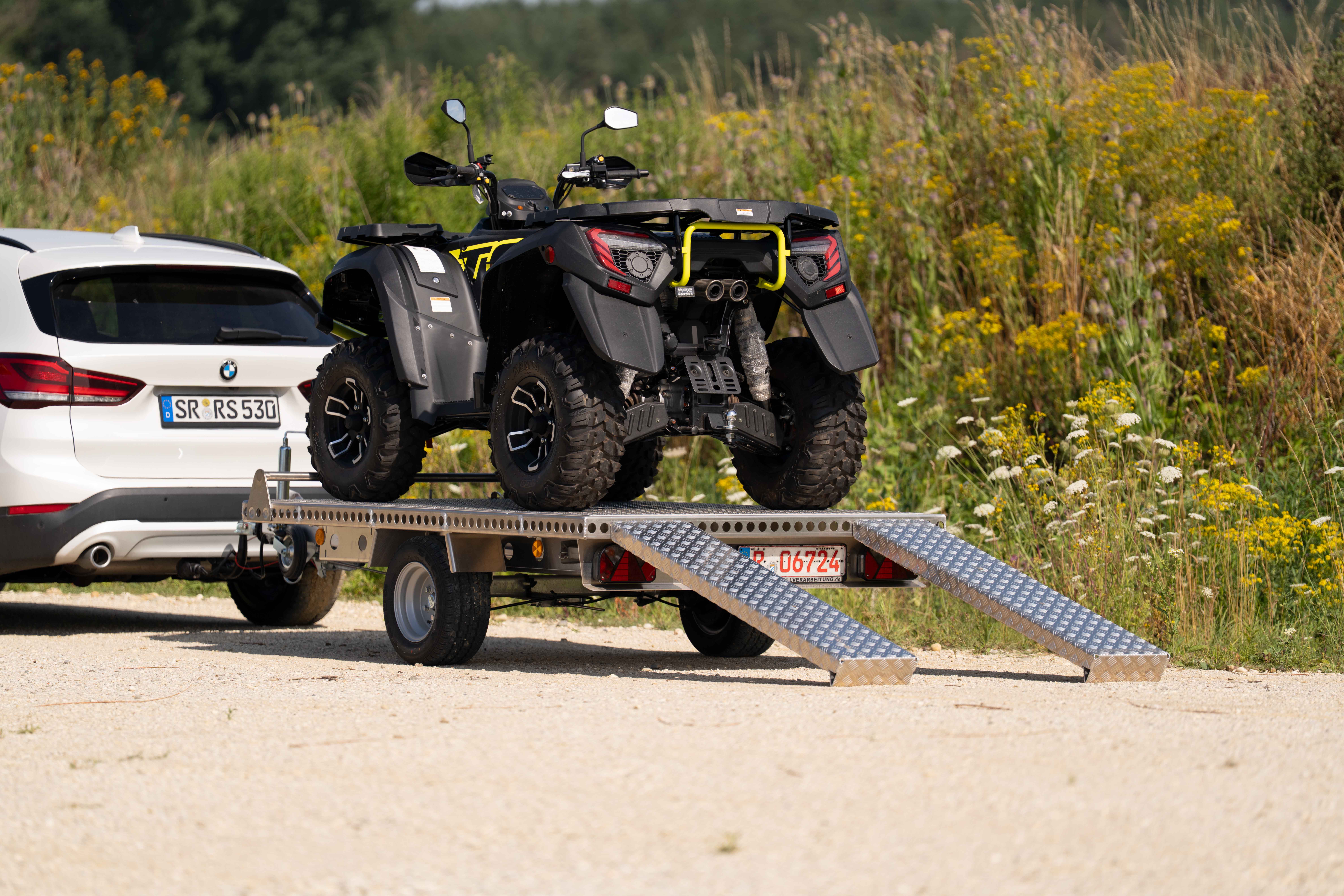 Aluminium Plattformanhänger mit einem Quad beladen hinter einem weißen Auto in einer Kiesgrube
