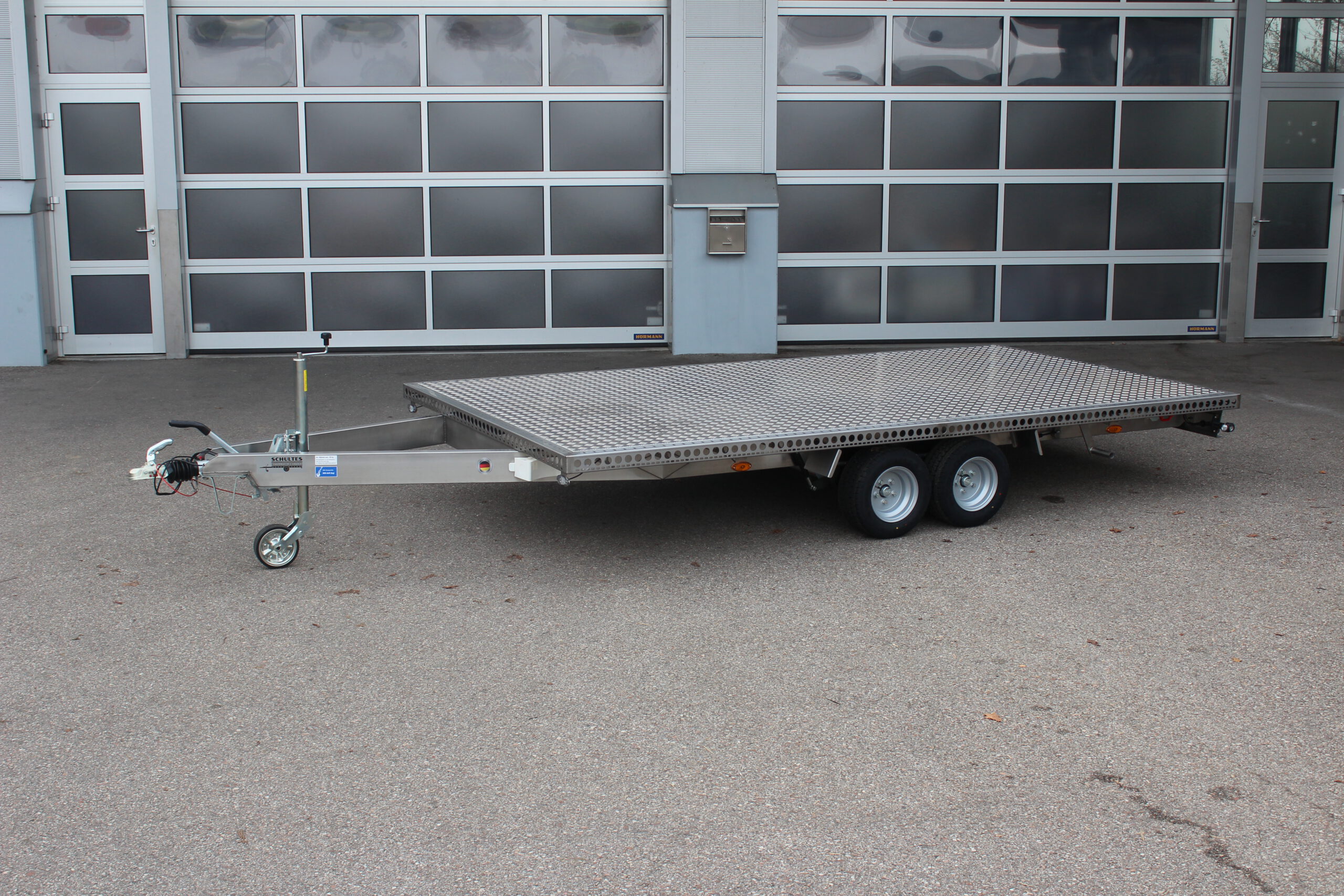 Zweiachs- Edelstahl Plattform-Anhänger, silber, vor einem Hallentor