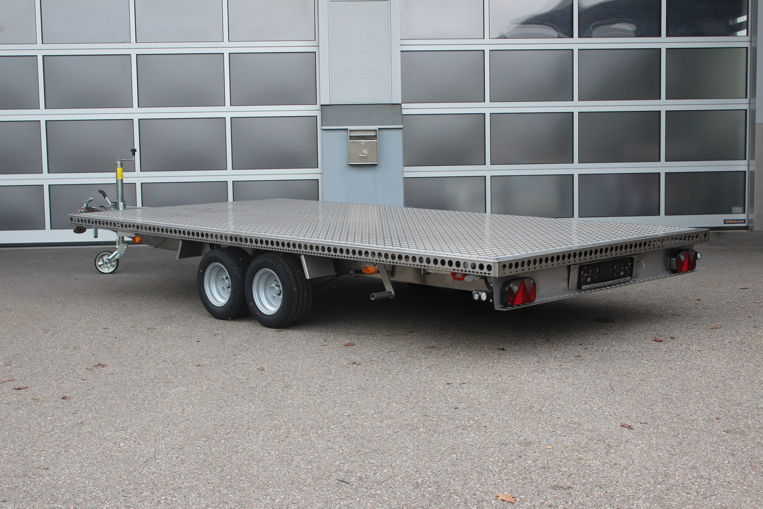 Zweiachs- Edelstahl Plattform-Anhänger, silber, vor einem Hallentor