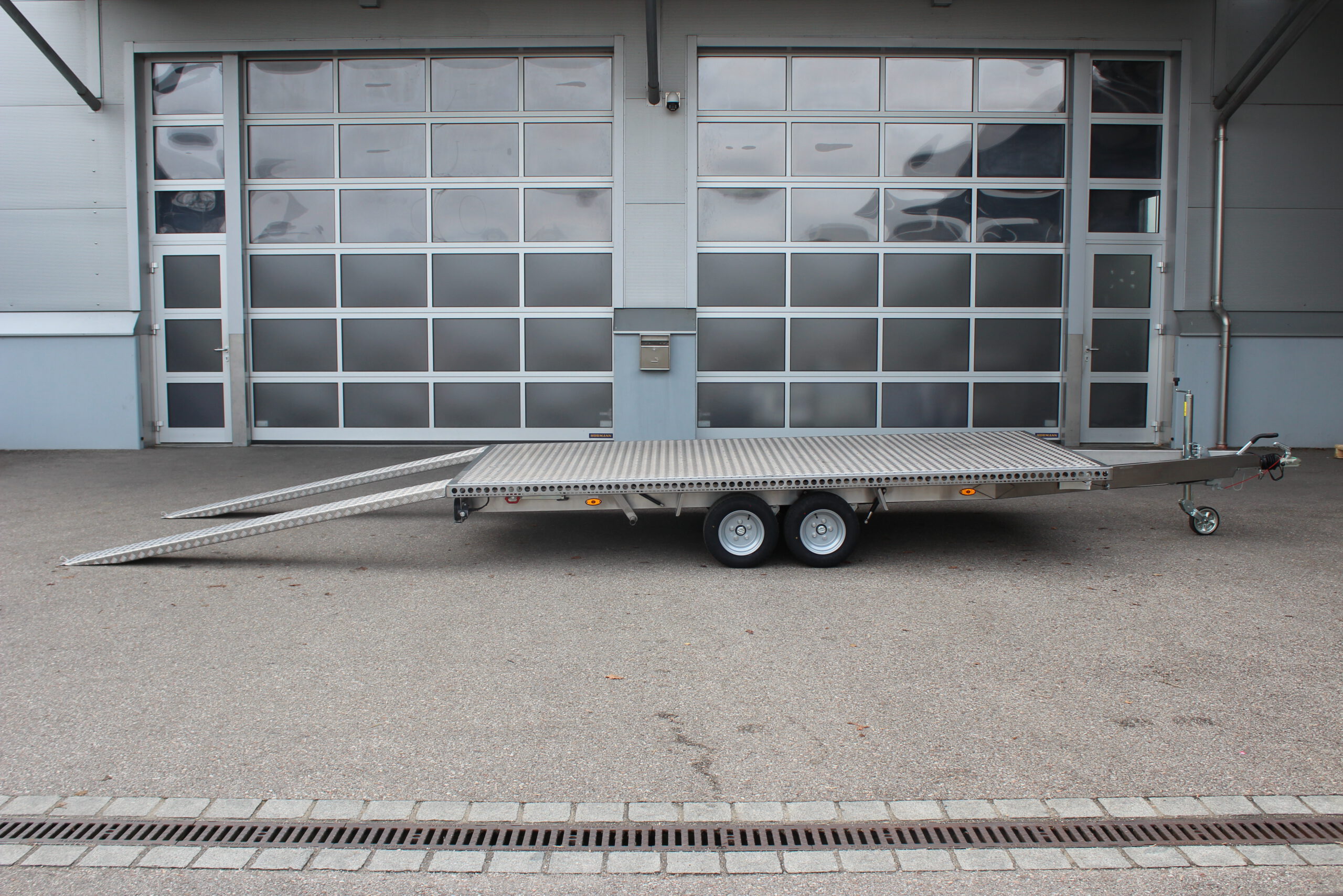 Zweiachs- Edelstahl Plattform-Anhänger, silber, vor einem Hallentor