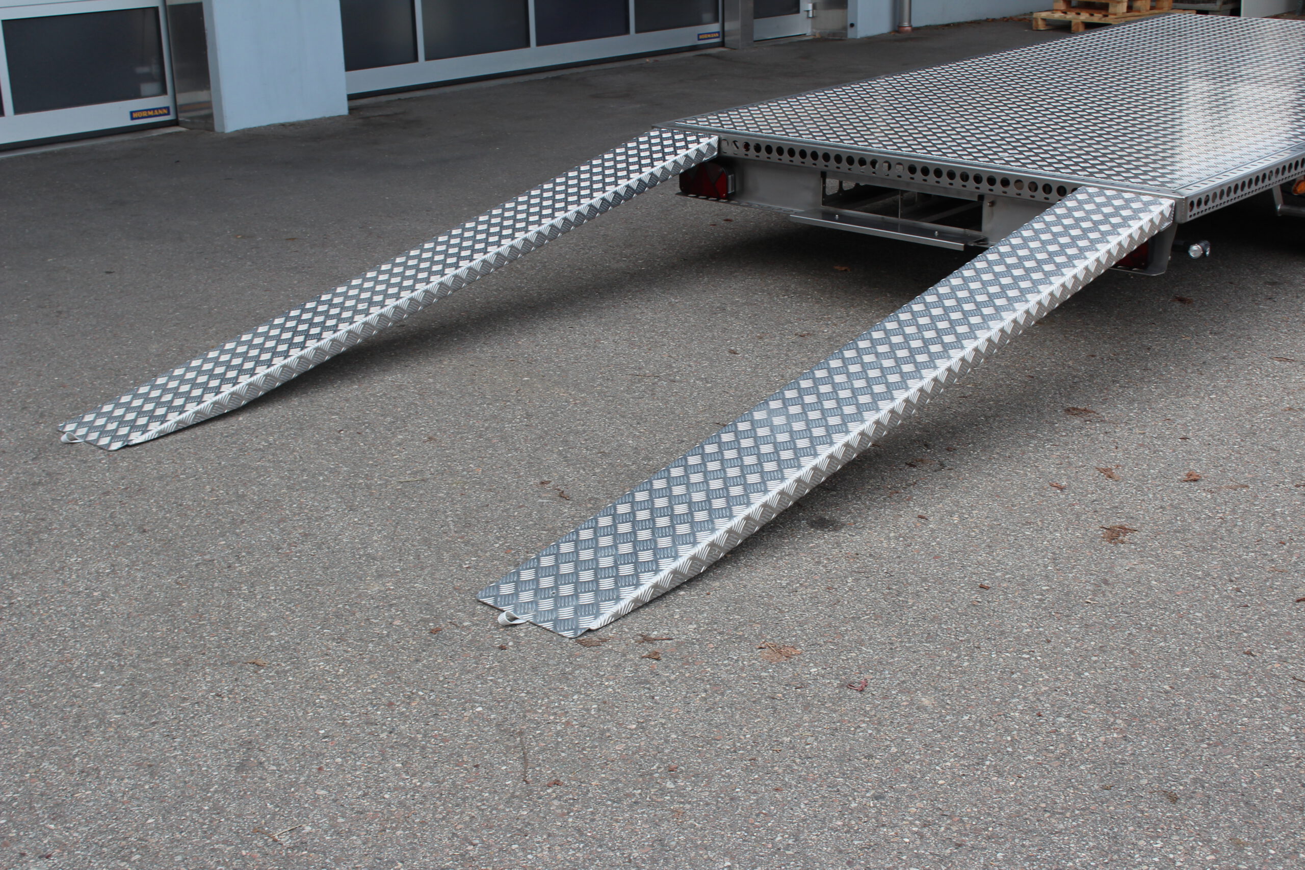 Zweiachs- Edelstahl Plattform-Anhänger, silber, vor einem Hallentor