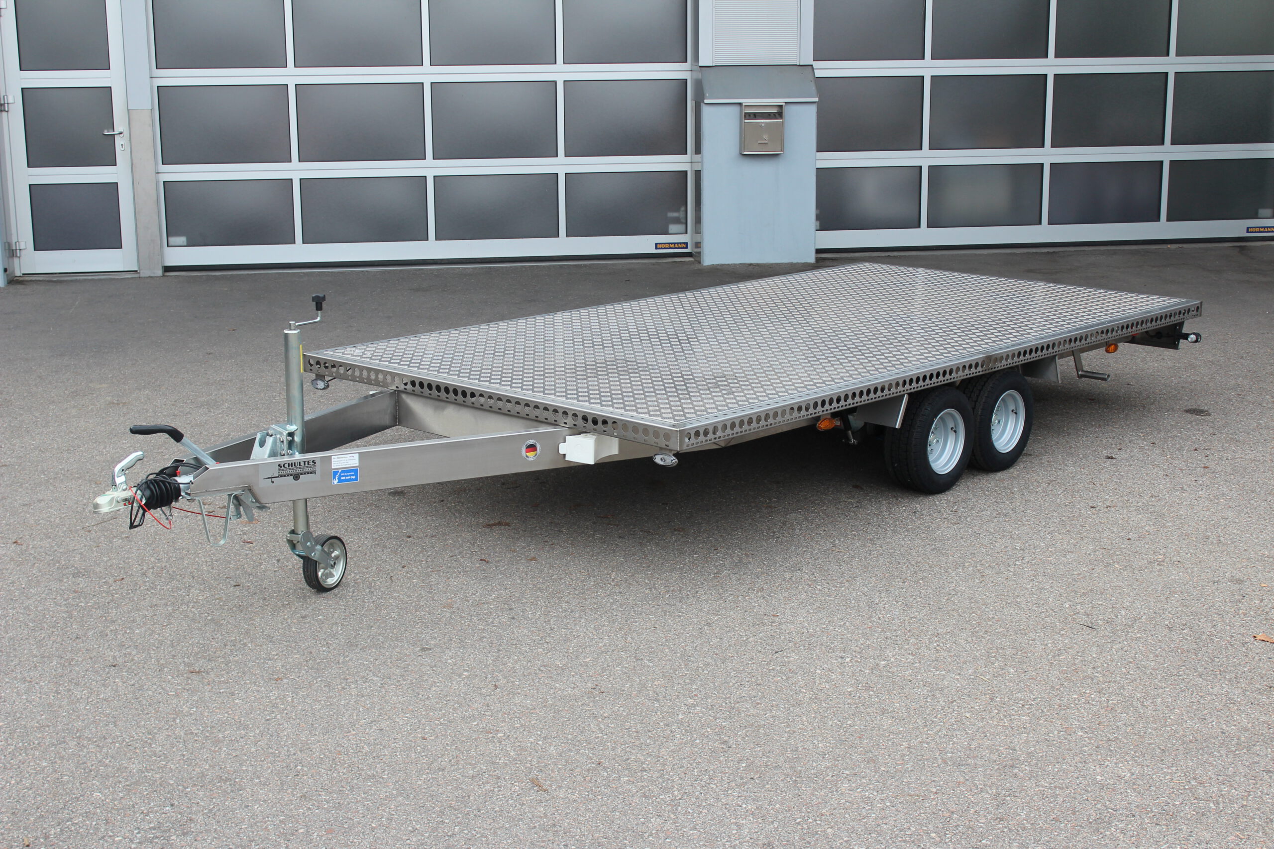 Zweiachs- Edelstahl Plattform-Anhänger, silber, vor einem Hallentor