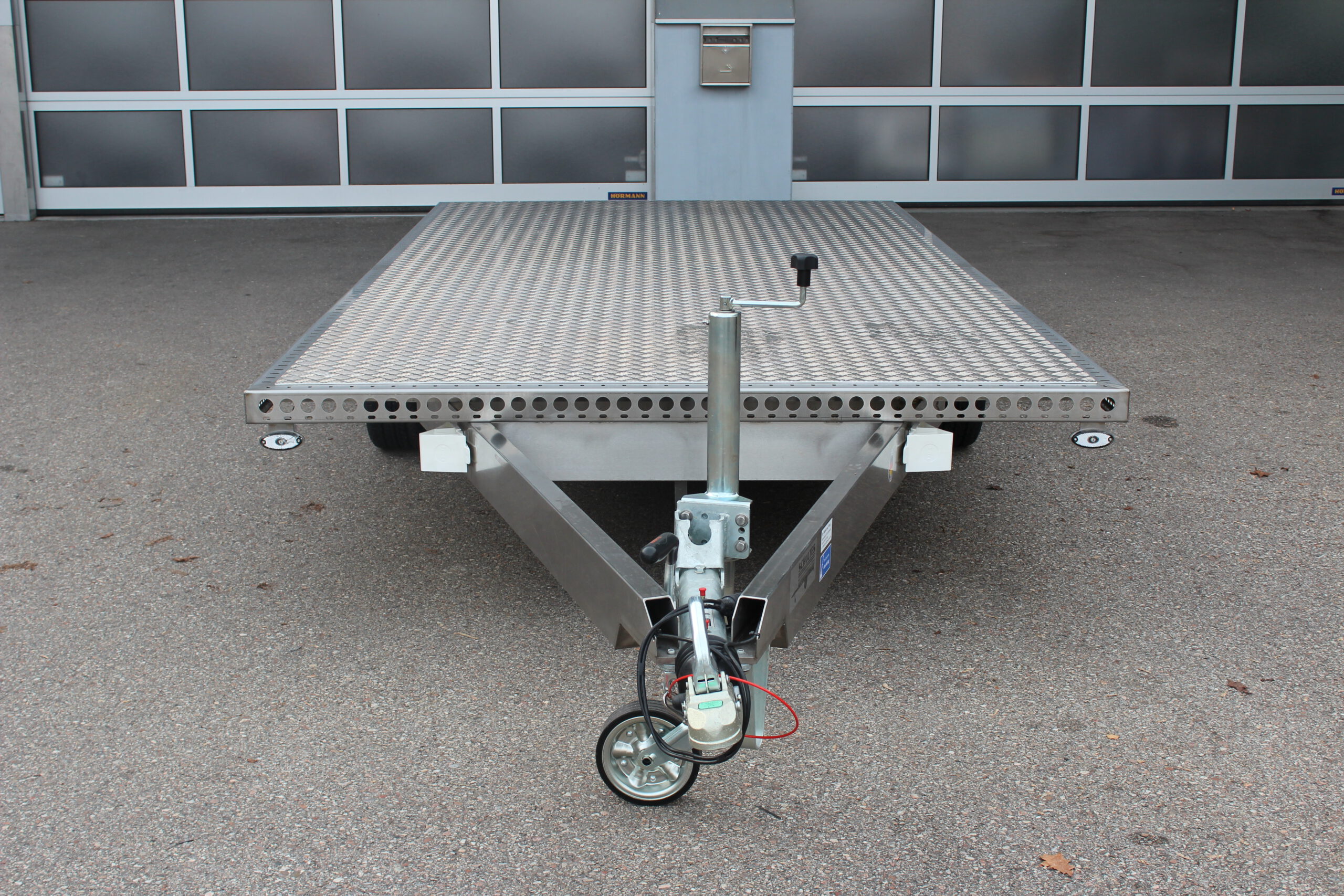 Zweiachs- Edelstahl Plattform-Anhänger, silber, vor einem Hallentor