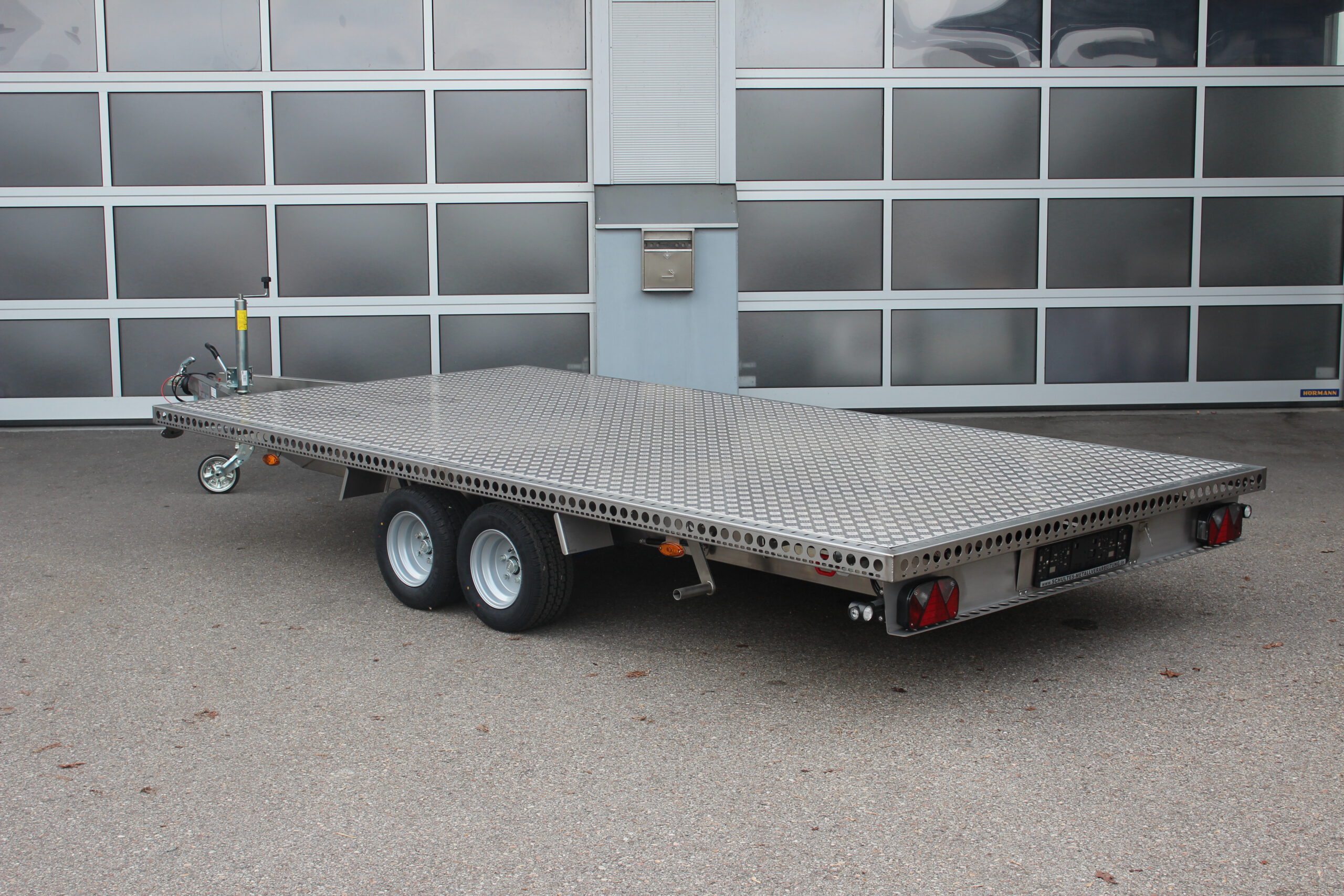 Zweiachs- Edelstahl Plattform-Anhänger, silber, vor einem Hallentor