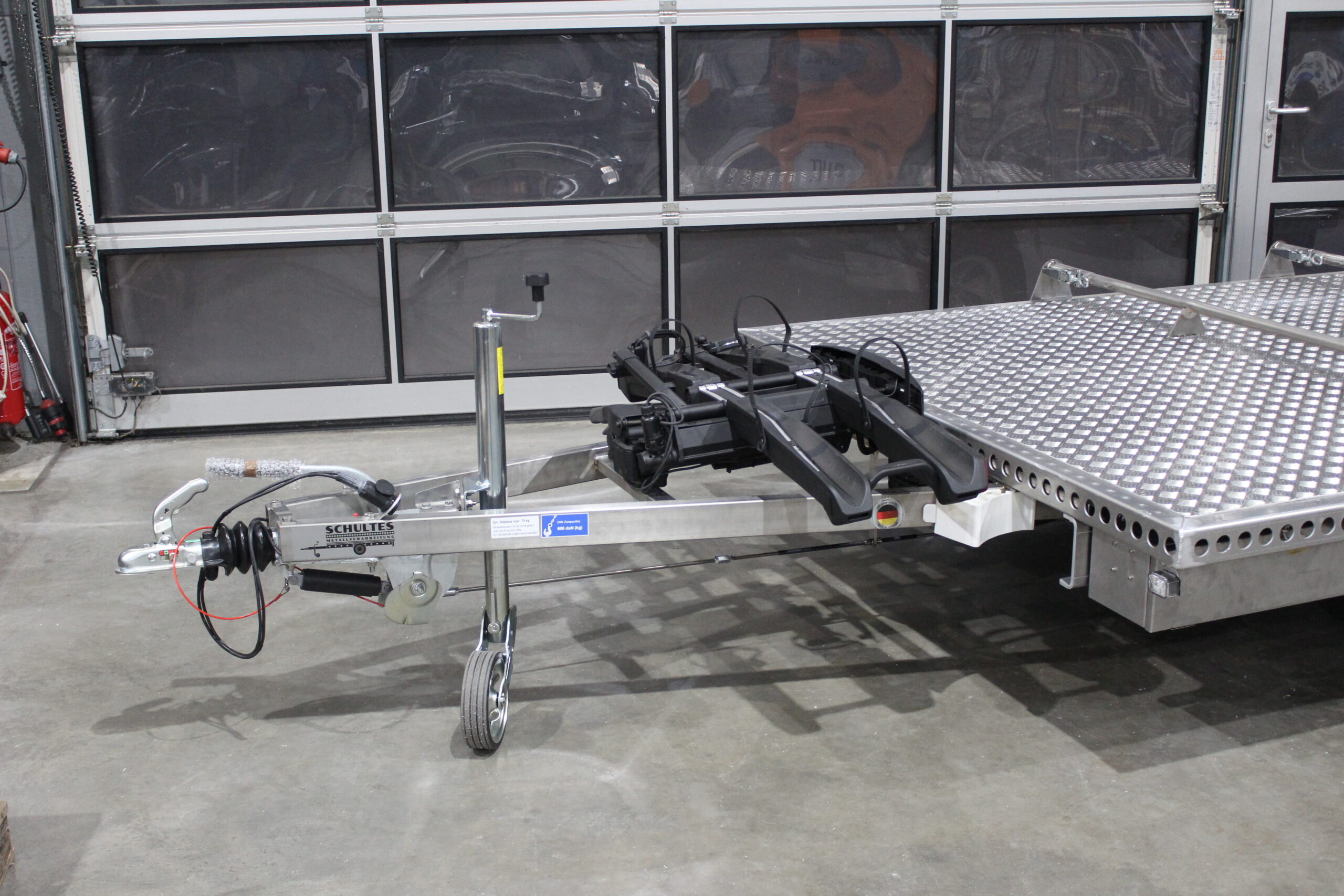Aluminium Plattformanhänger mit verlängerter Zugdeichsel und Fahrradträger auf der Deichsel in einer Halle vor einem Tor