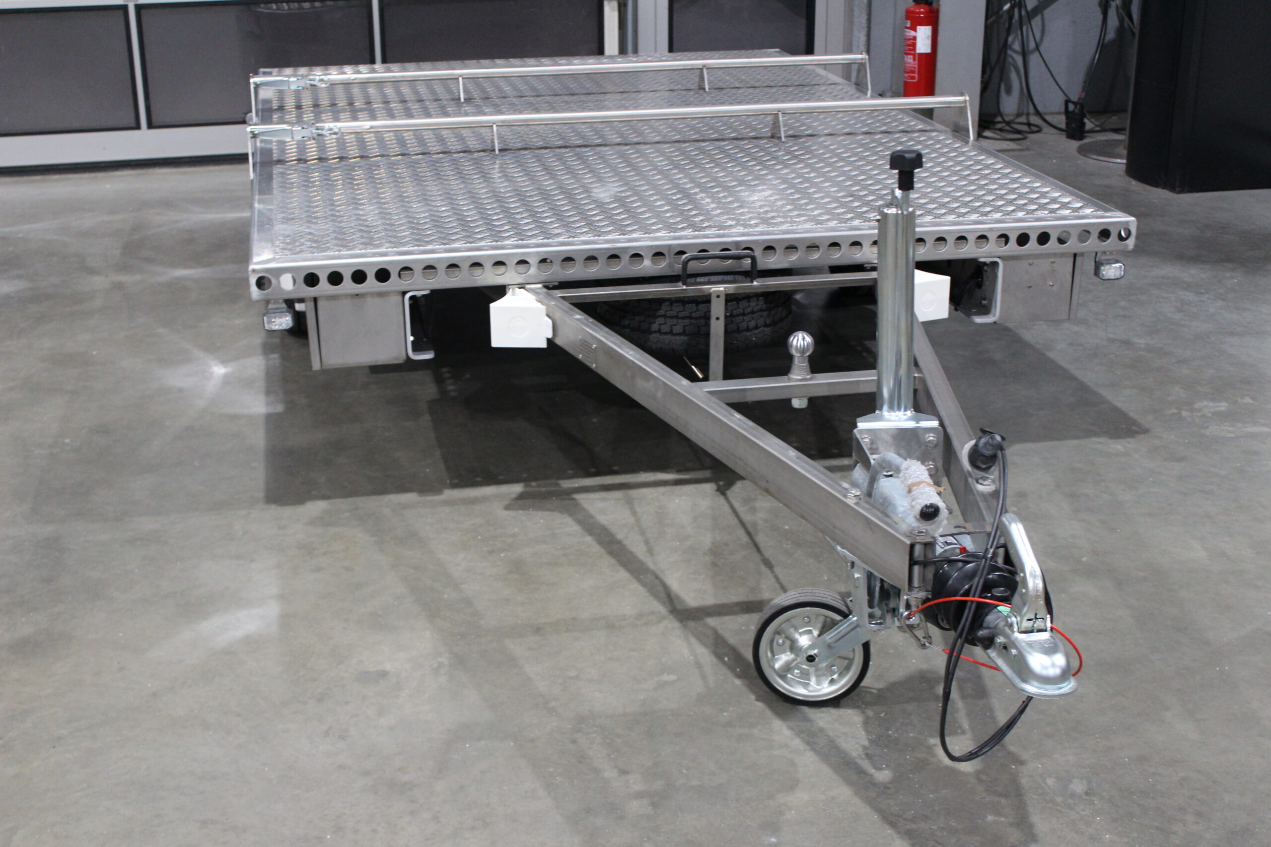 Aluminium Plattformanhänger mit verlängerter Zugdeichsel und einer Kupplungskugel in der Deichsel für einen Fahrradträger in einer Halle vor einem Tor