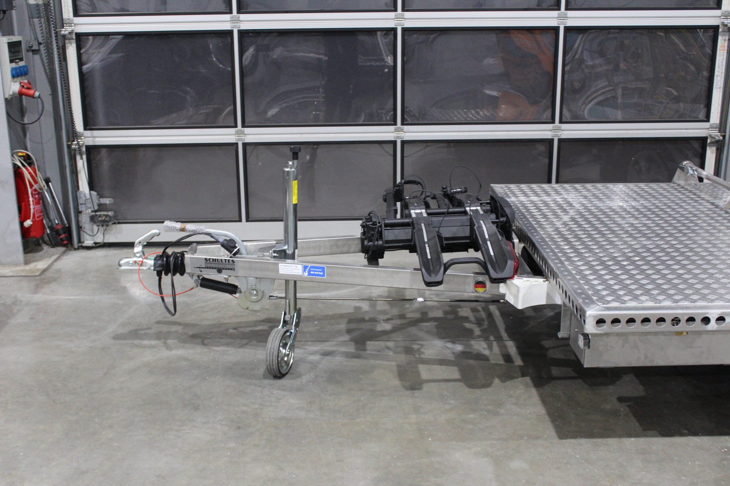 Aluminium Plattformanhänger mit verlängerter Zugdeichsel und Fahrradträger auf der Deichsel in einer Halle vor einem Tor