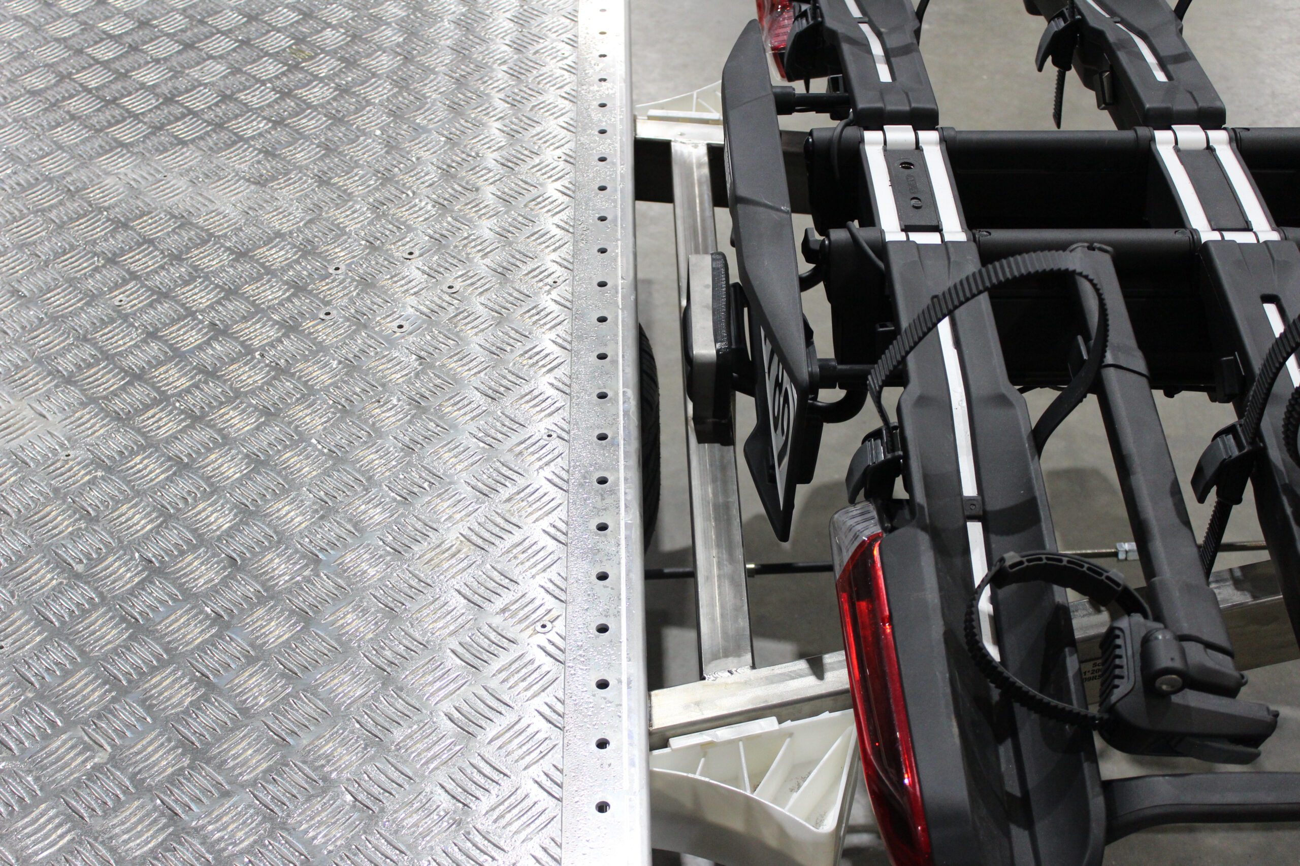 Aluminium Plattformanhänger mit verlängerter Zugdeichsel und Fahrradträger auf der Deichsel in einer Halle vor einem Tor