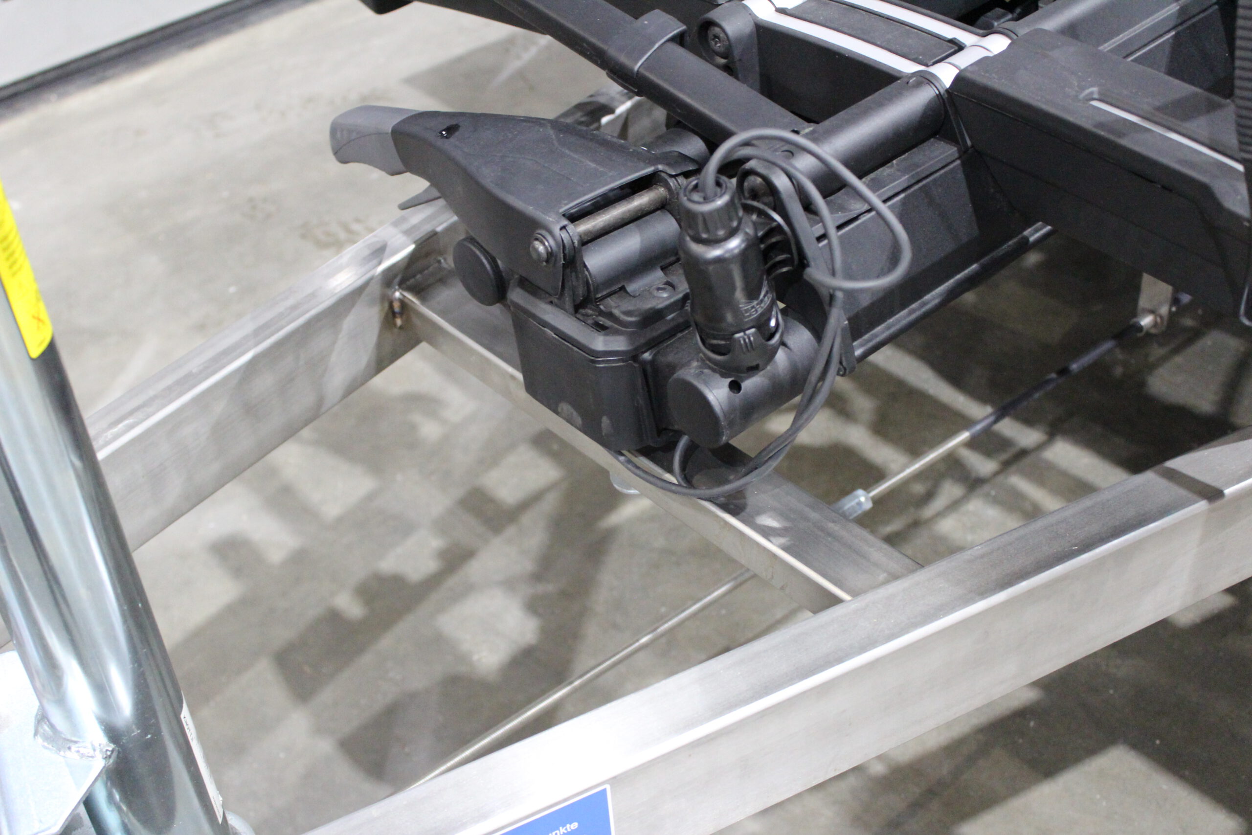 Aluminium Plattformanhänger mit verlängerter Zugdeichsel und Fahrradträger auf der Deichsel in einer Halle vor einem Tor