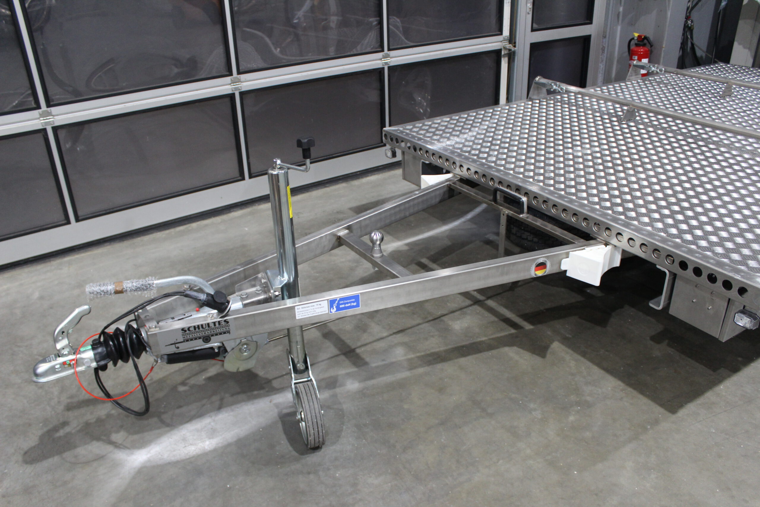 Aluminium Plattformanhänger mit verlängerter Zugdeichsel und einer Kupplungskugel in der Deichsel für einen Fahrradträger in einer Halle vor einem Tor