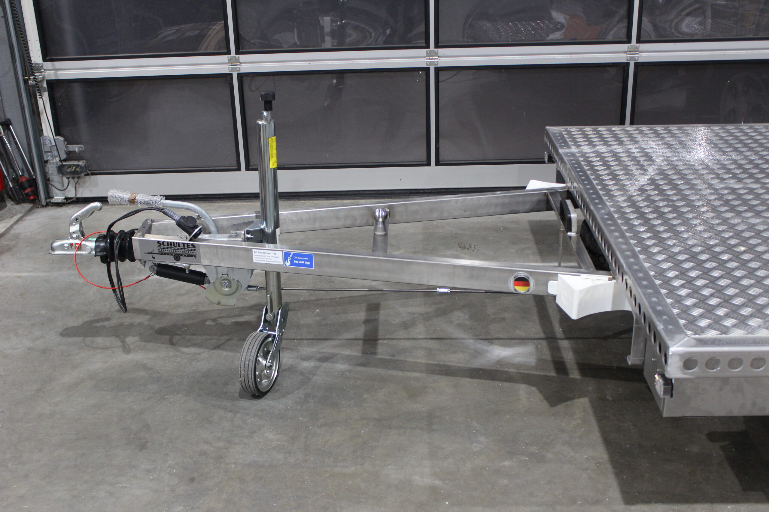 Aluminium Plattformanhänger mit verlängerter Zugdeichsel und einer Kupplungskugel in der Deichsel für einen Fahrradträger in einer Halle vor einem Tor
