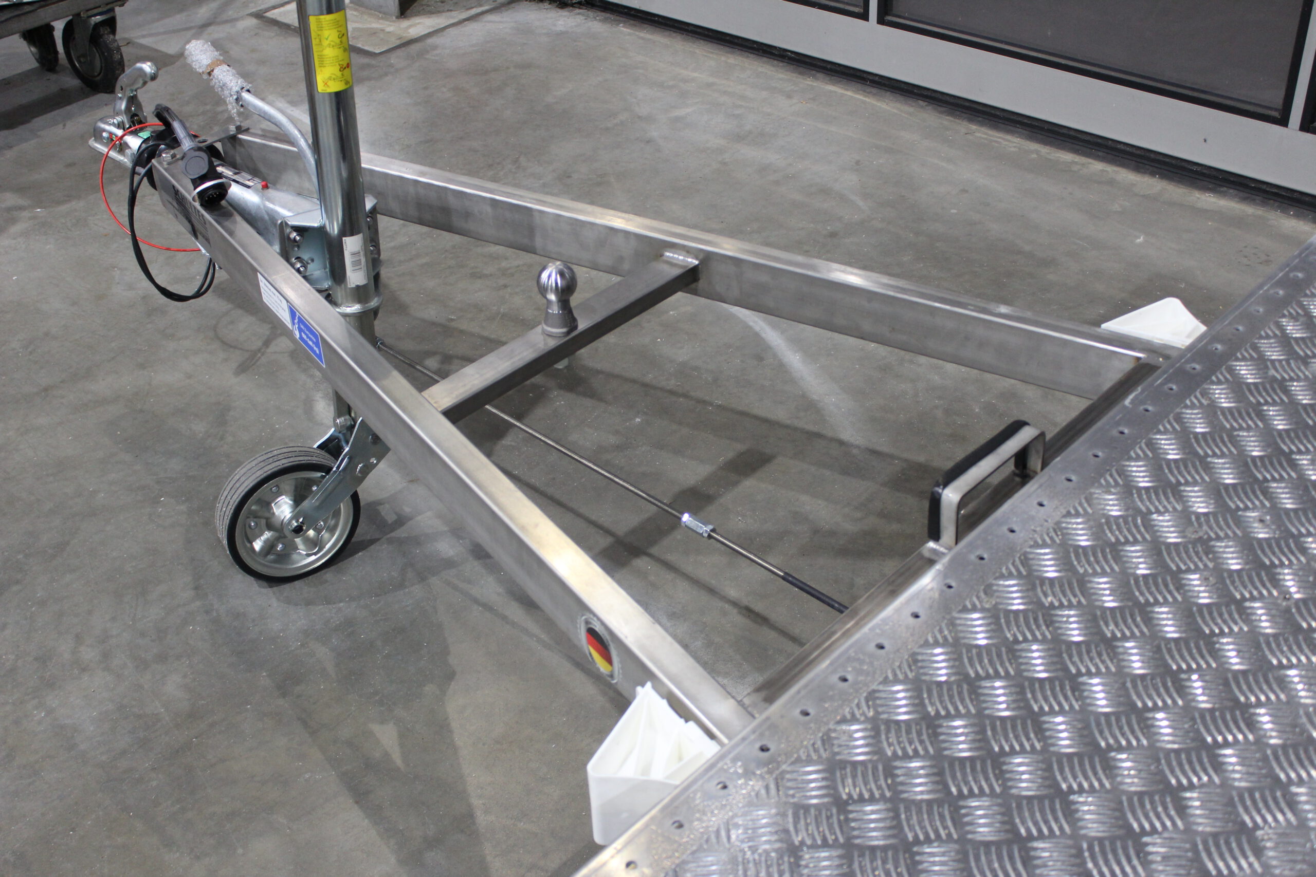 Aluminium Plattformanhänger mit verlängerter Zugdeichsel und einer Kupplungskugel in der Deichsel für einen Fahrradträger in einer Halle vor einem Tor