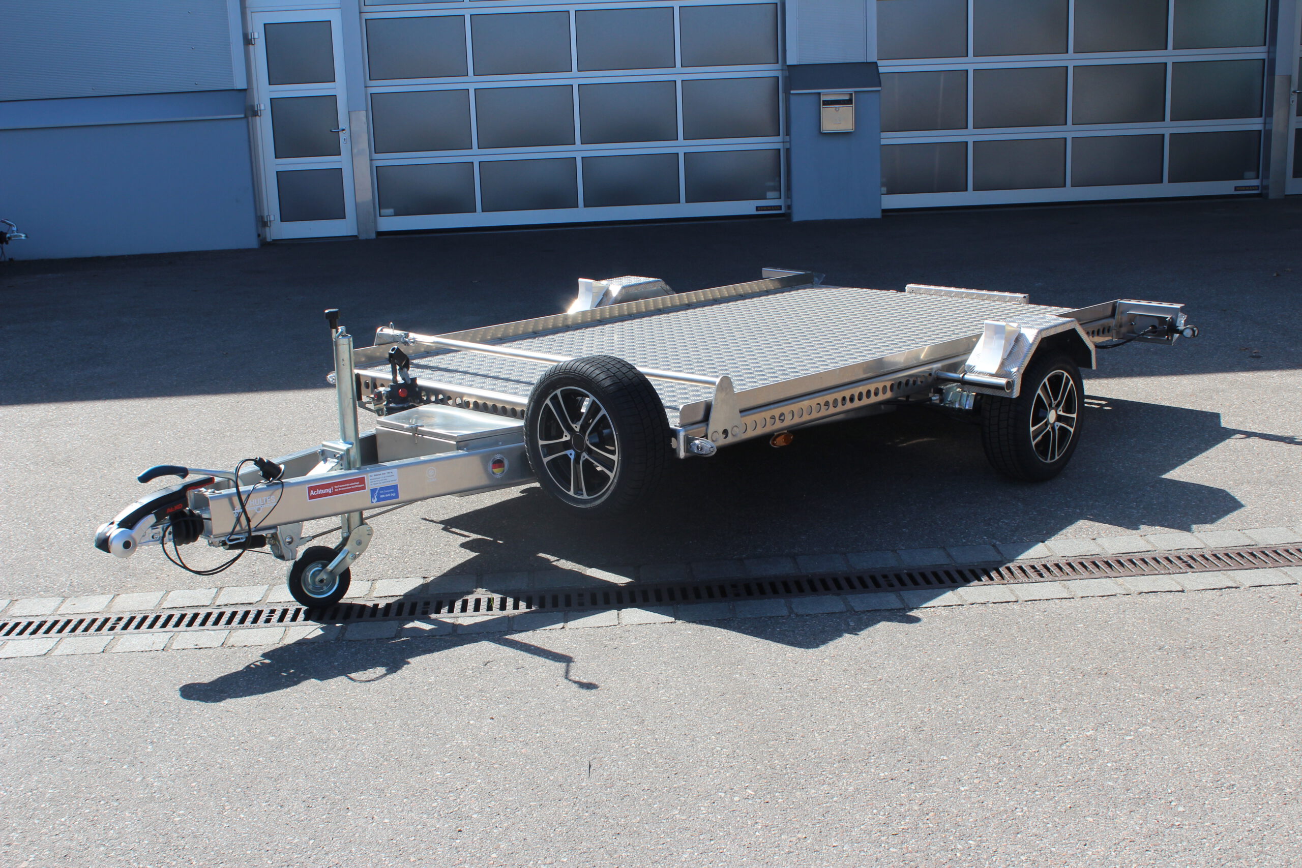 Absenkanhänger aus Aluminium mit elektrischer Pumpe zum absenken und aufheben, mit Alufelgen, Ersatzrad, Antischlingerkupplung vor einer Halle auf einem Hof