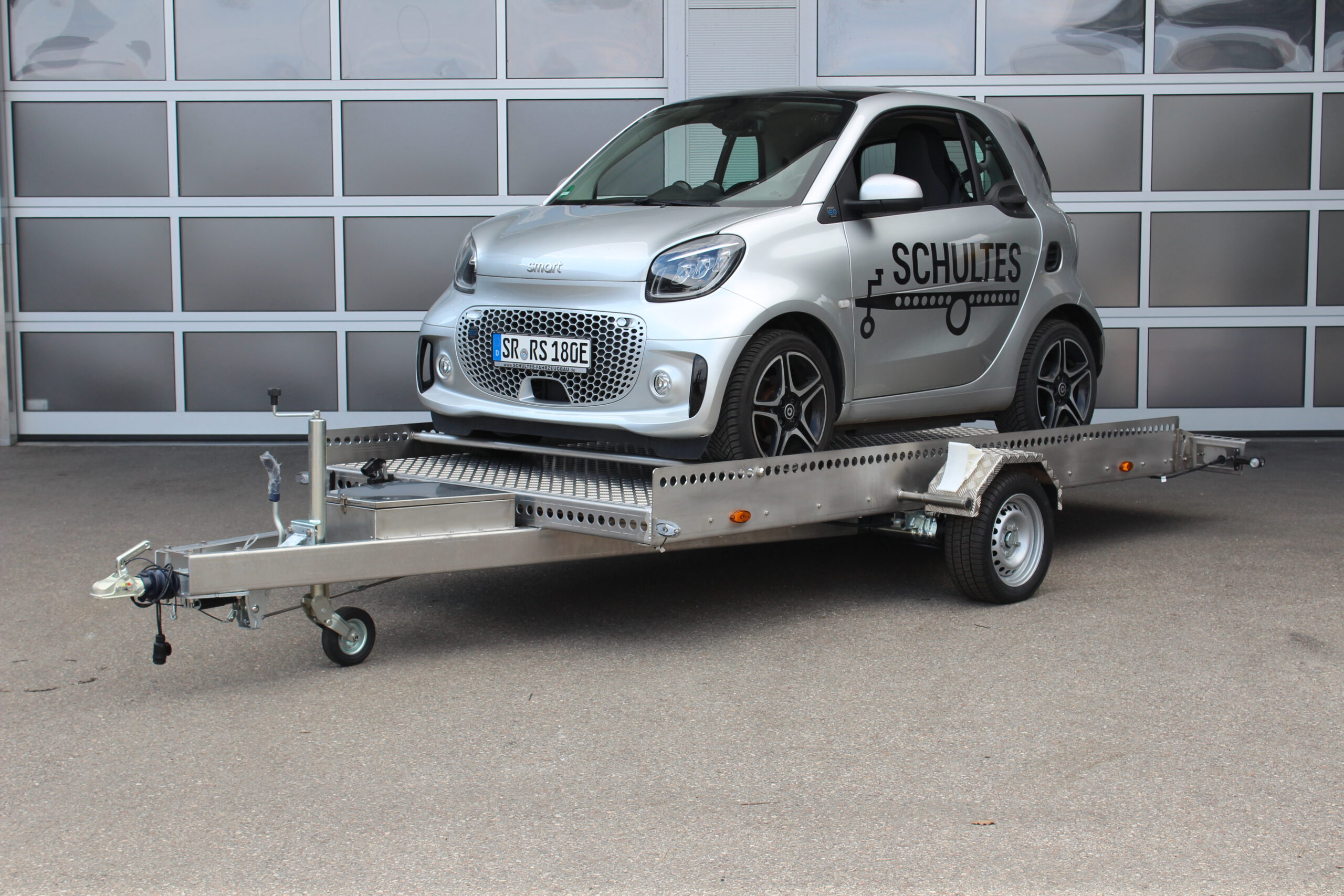 AS400 Absenkanhänger aus Aluminium und Edelstahl mit einem Smart beladen vor einer Halle