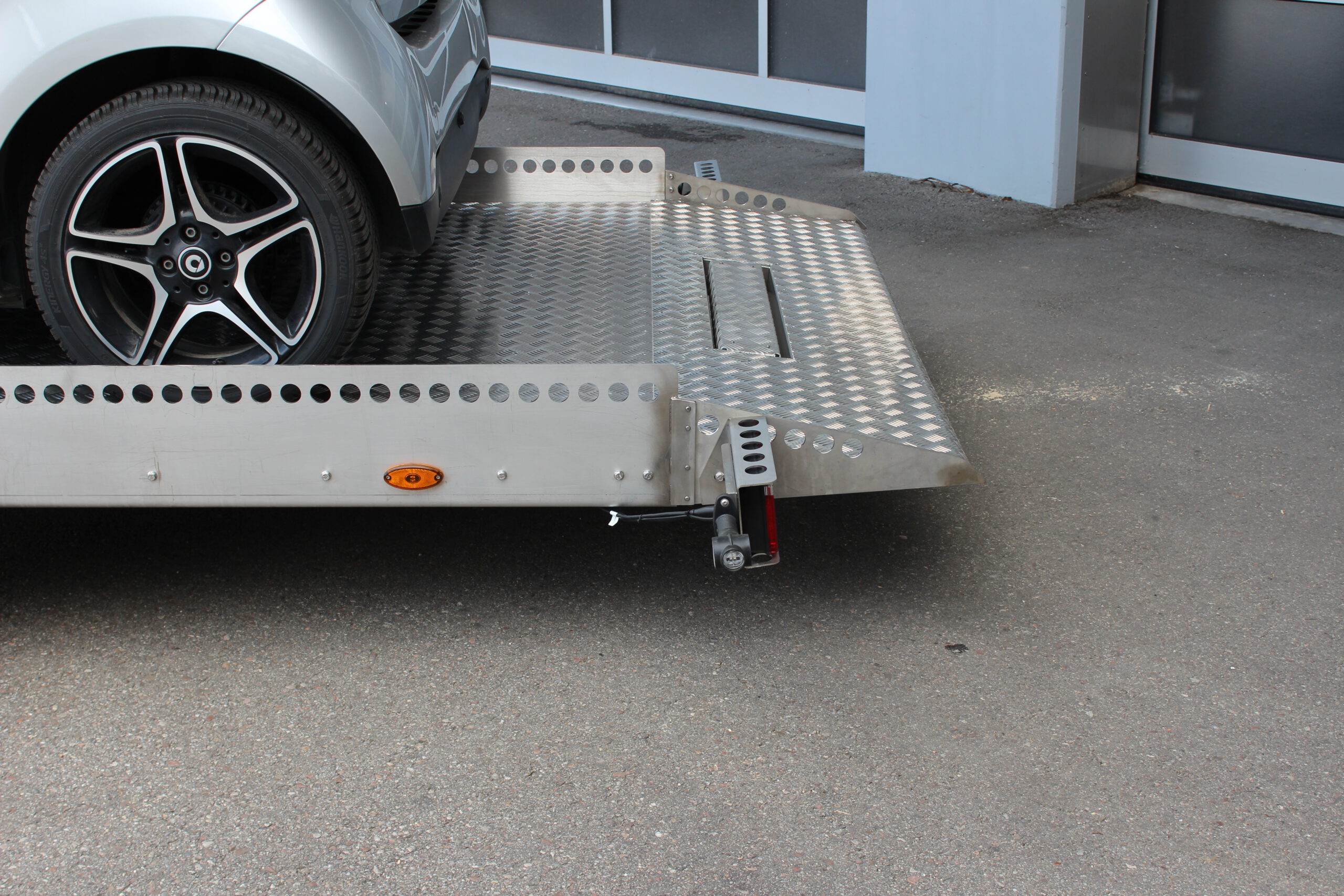 AS400 Absenkanhänger aus Aluminium und Edelstahl mit einem Smart beladen vor einer Halle