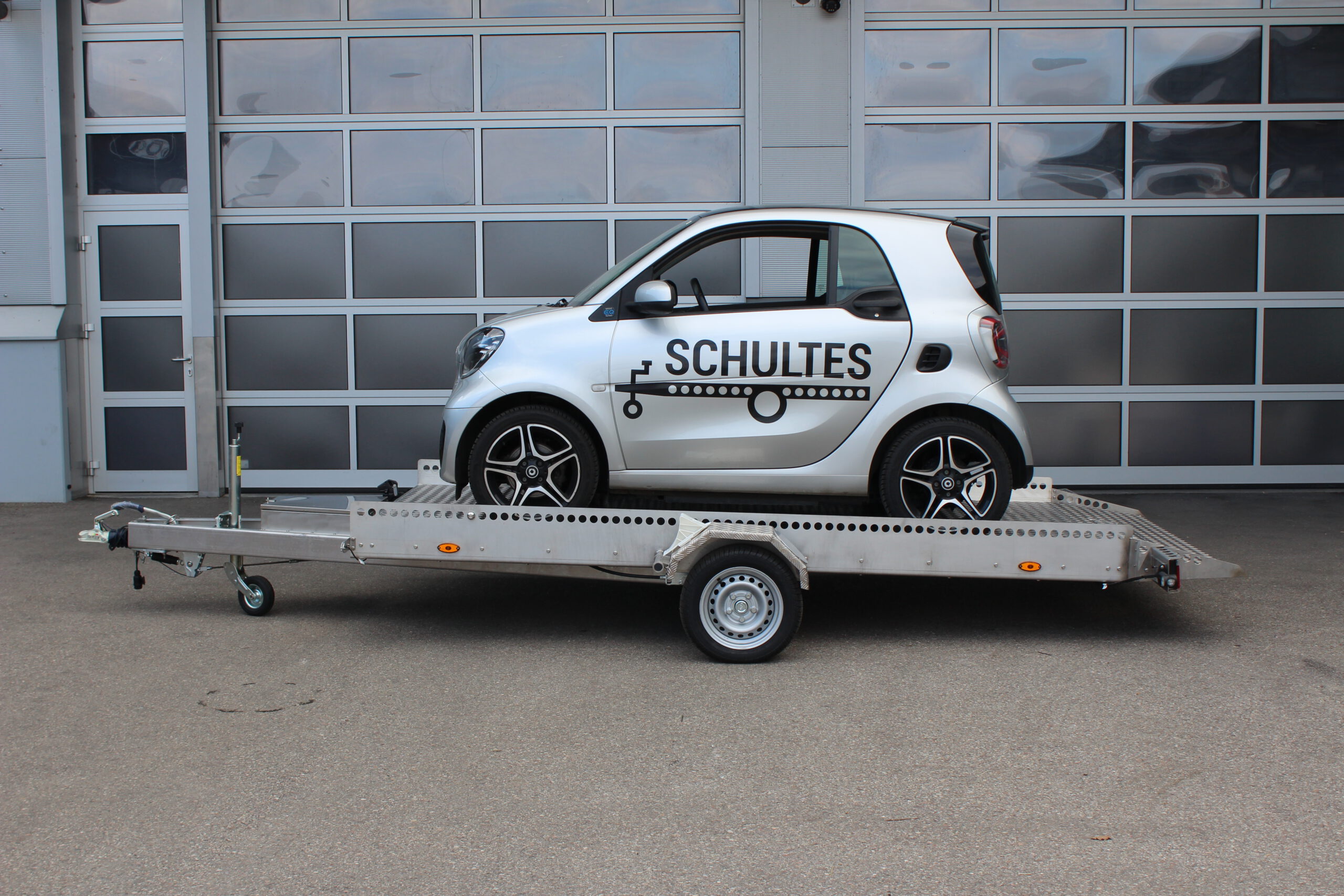 AS400 Absenkanhänger aus Aluminium und Edelstahl mit einem Smart beladen vor einer Halle