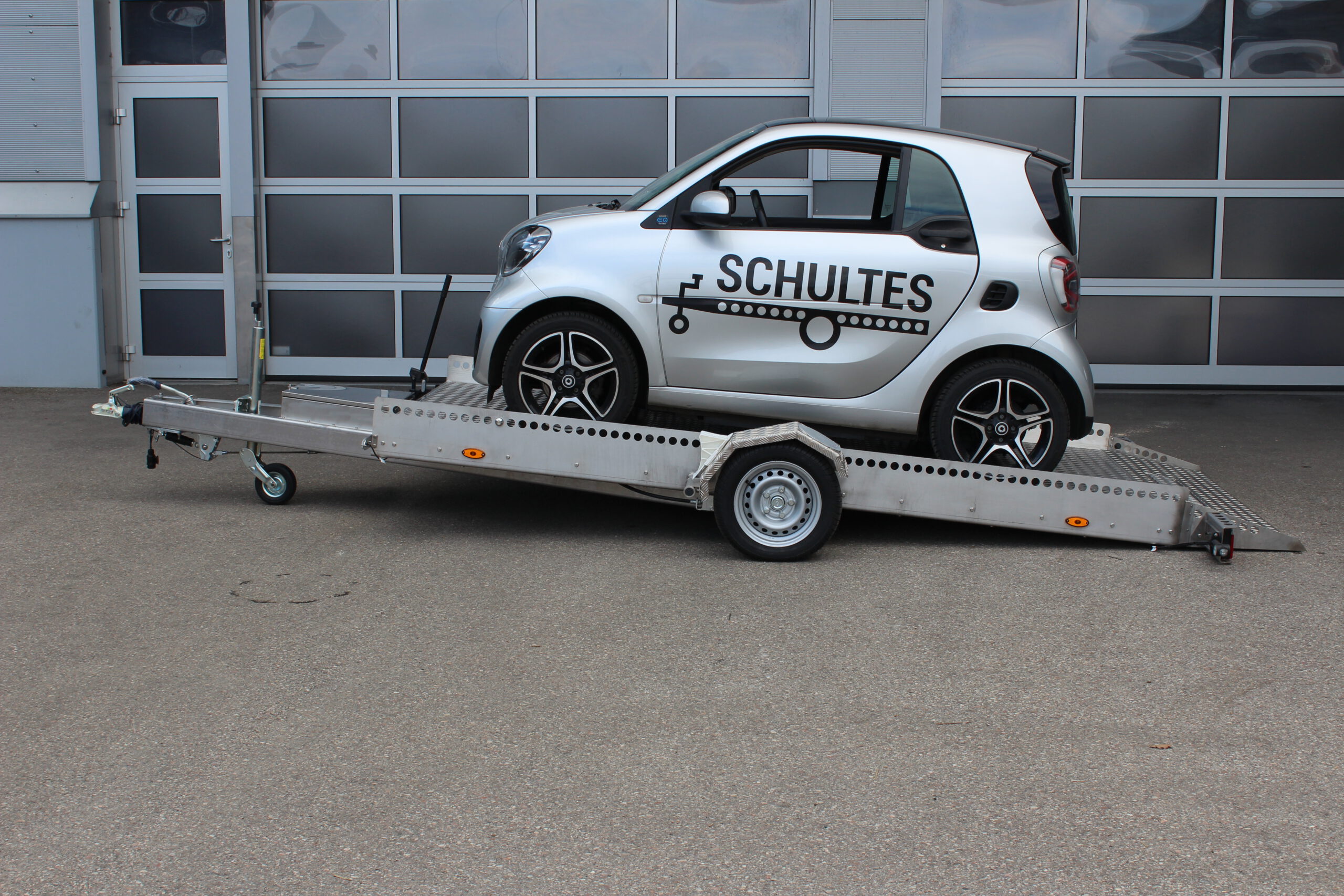 AS400 Absenkanhänger aus Aluminium und Edelstahl mit einem Smart beladen vor einer Halle