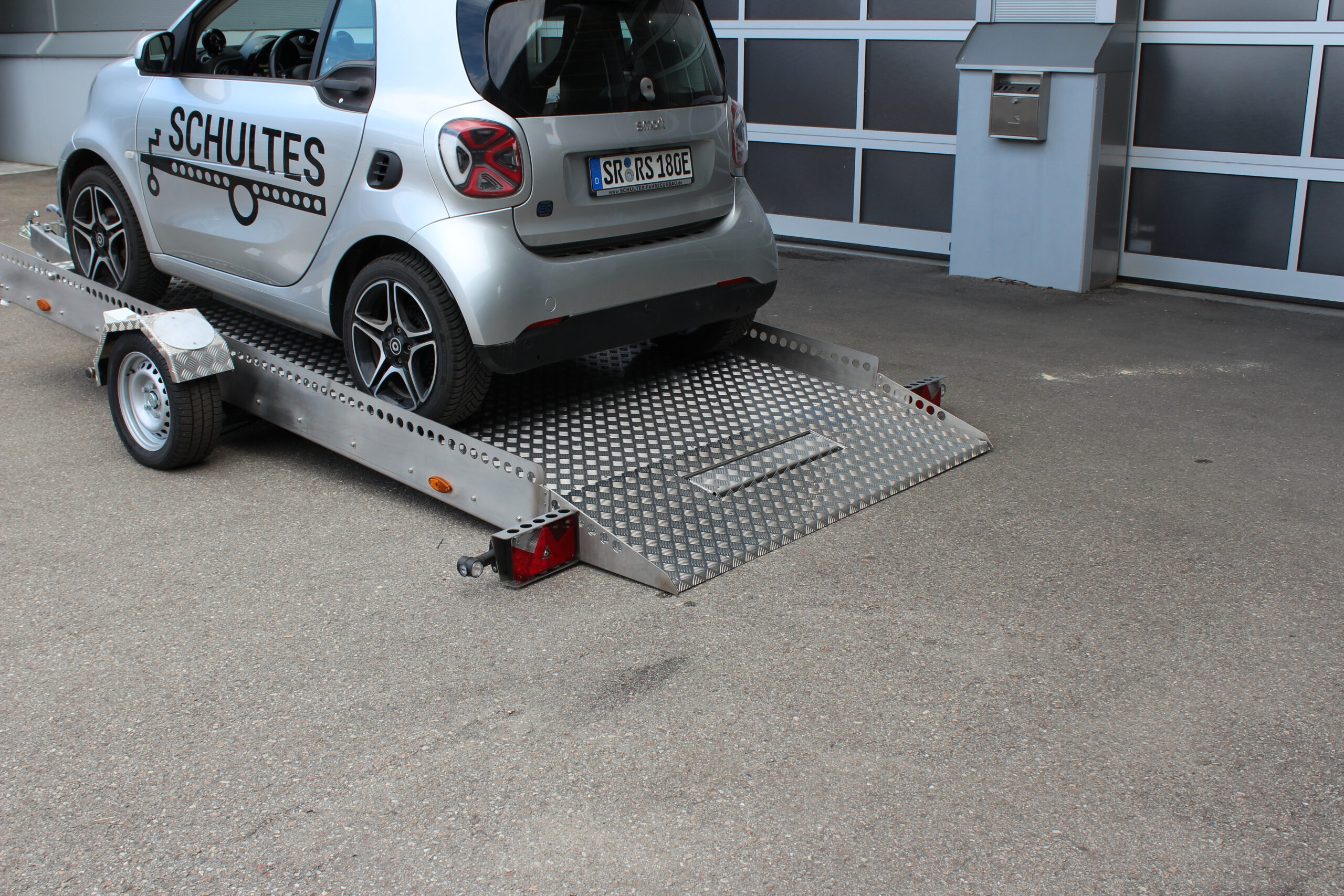AS400 Absenkanhänger aus Aluminium und Edelstahl mit einem Smart beladen vor einer Halle