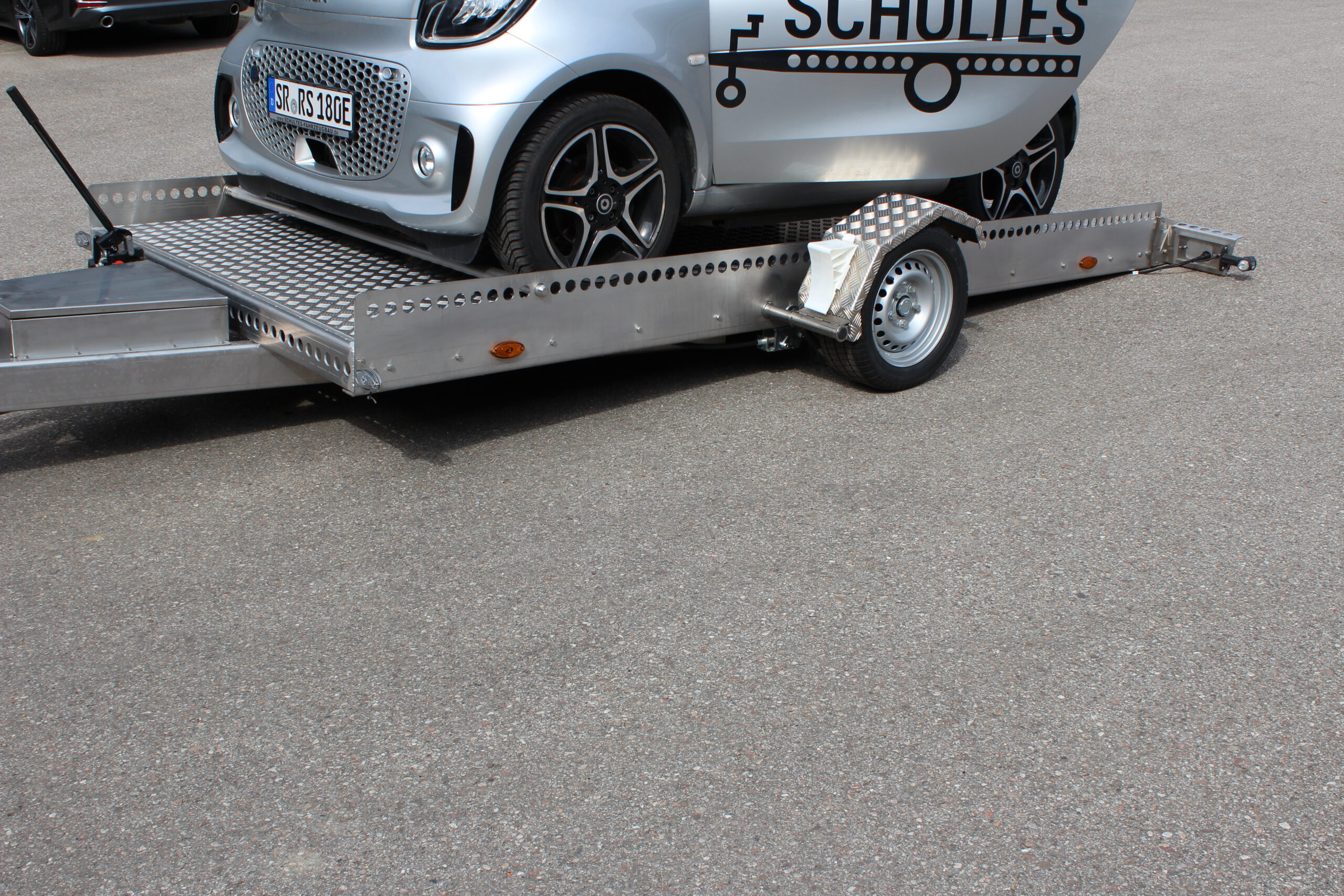 AS400 Absenkanhänger aus Aluminium und Edelstahl mit einem Smart beladen vor einer Halle