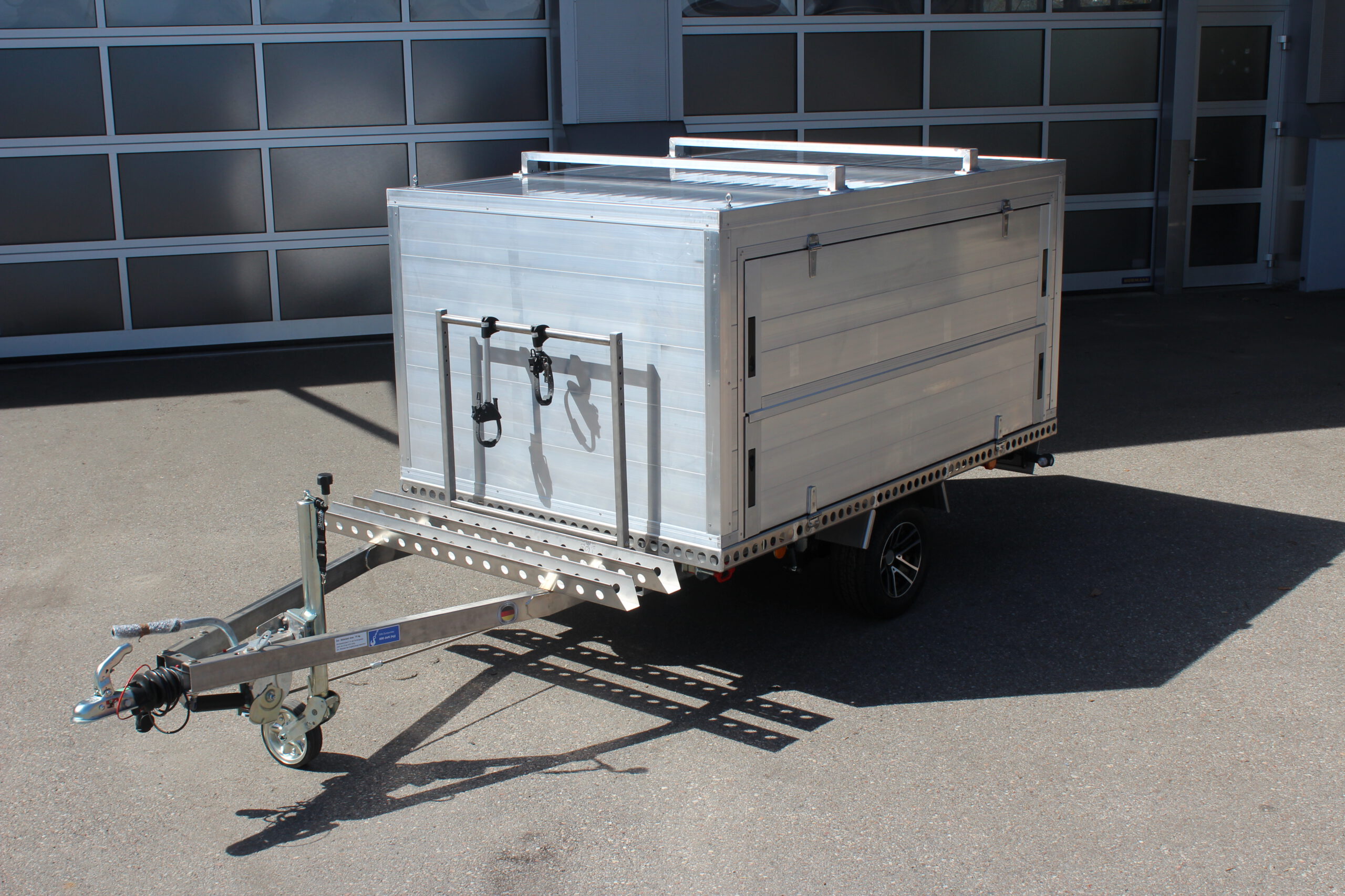 Fahrradträger für 2 Fahrräder aus Edelstahl an einem Kofferanhänger vor einer Halle