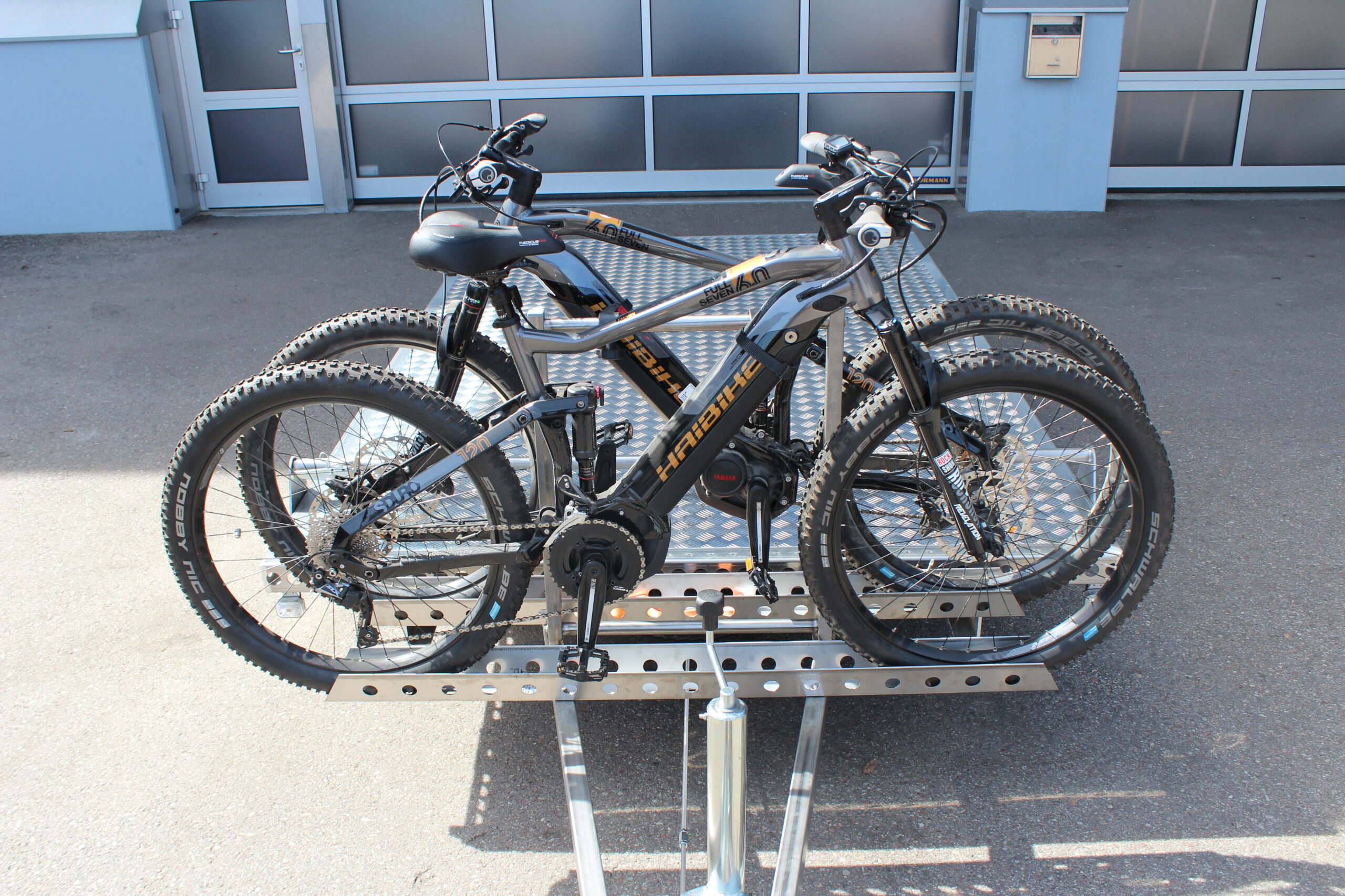 Fahrradträger für 2 Fahrräder aus Edelstahl an einem Anhänger befestigt mit 2 E-Bikes beladen vor einer Halle