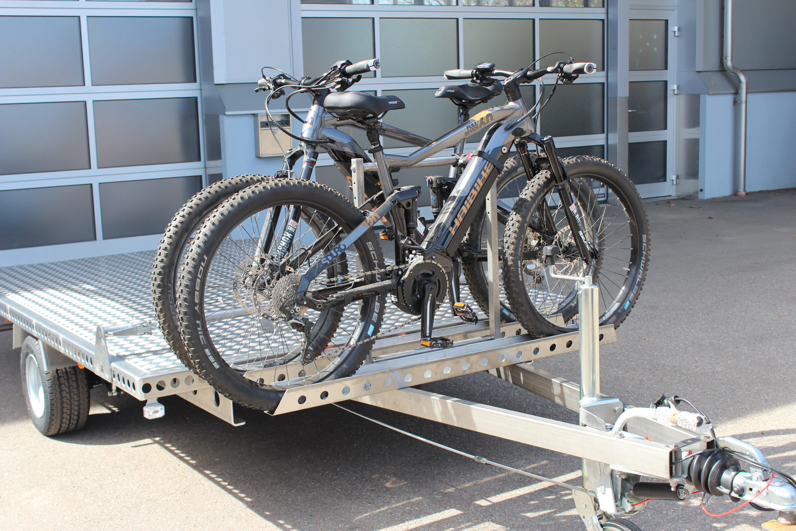 Fahrradträger für 2 Fahrräder aus Edelstahl an einem Anhänger befestigt mit 2 E-Bikes beladen vor einer Halle