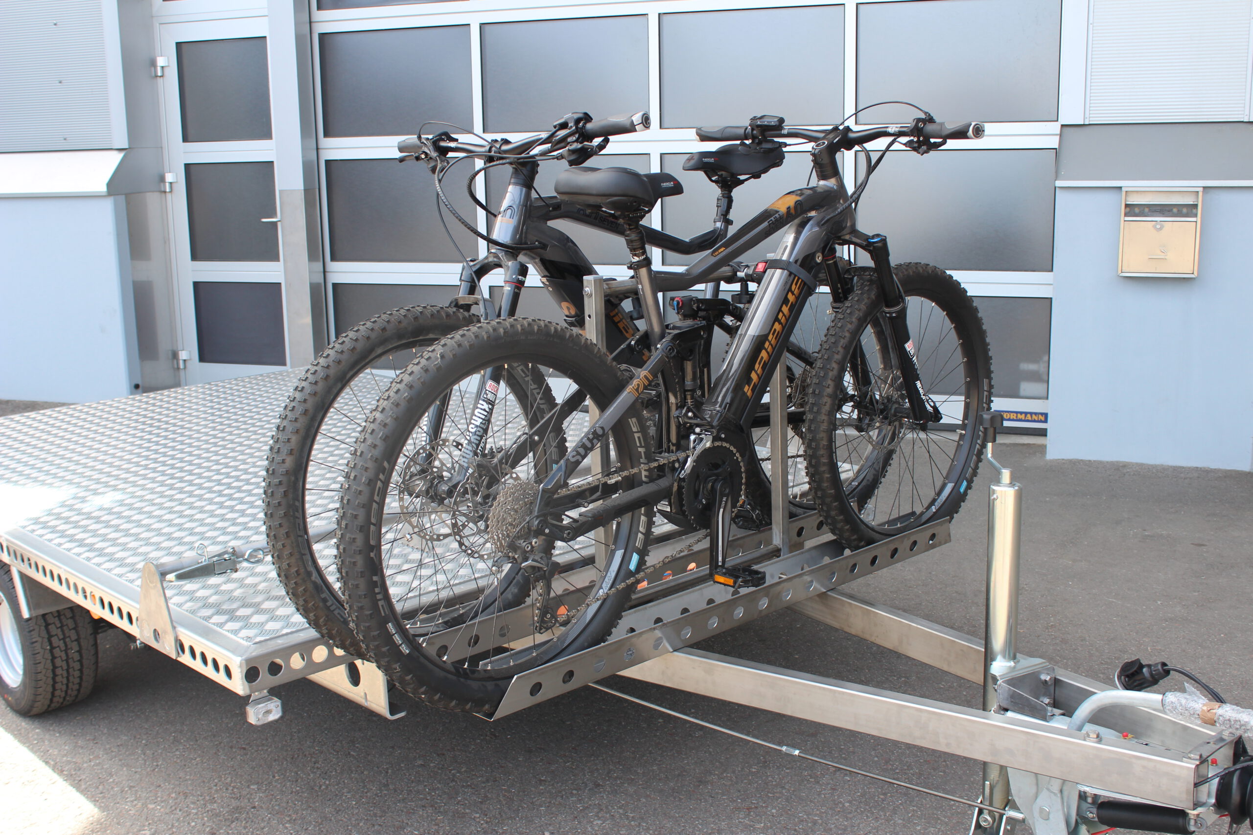 Fahrradträger für 2 Fahrräder aus Edelstahl an einem Anhänger befestigt mit 2 E-Bikes beladen vor einer Halle