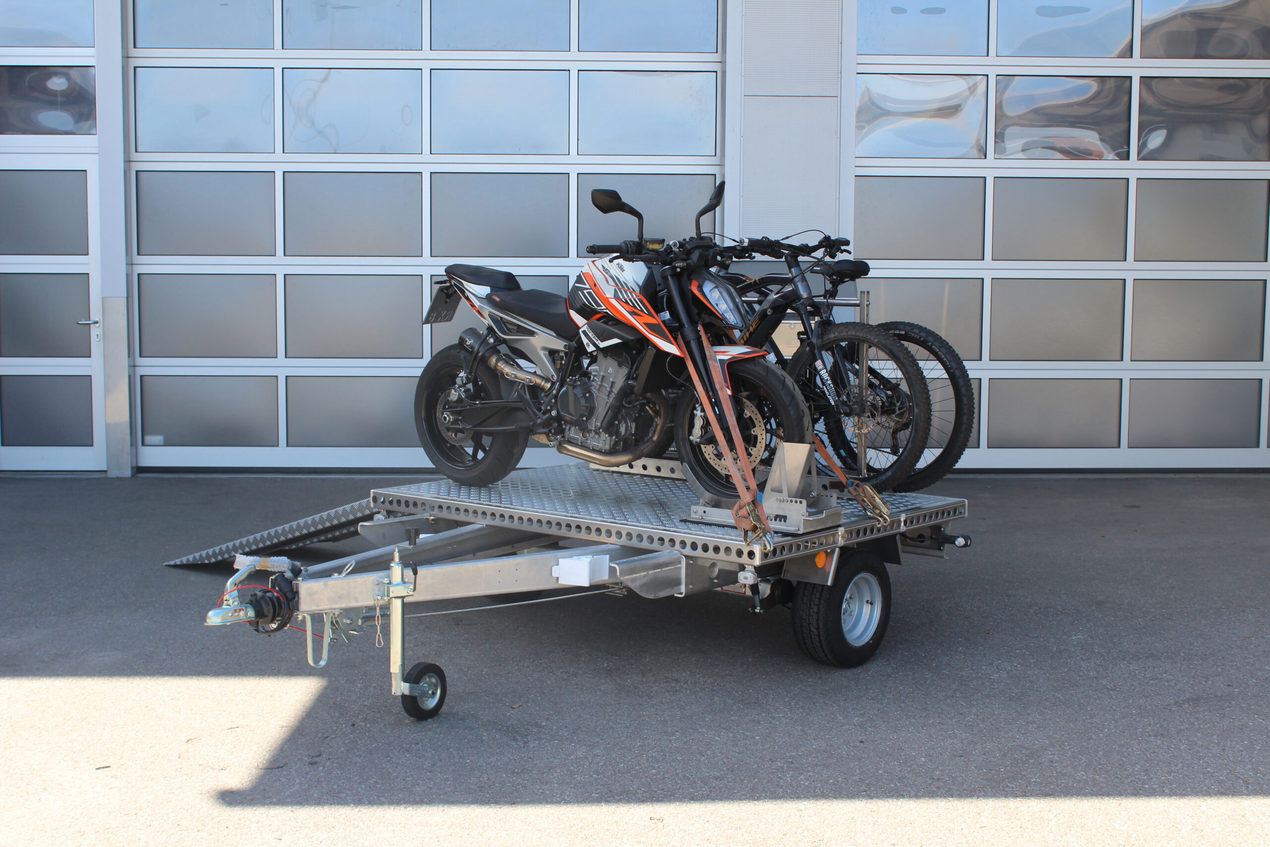 UA150 Quer Anhänger mit einer KTM Duke und zwei Fahrrädern beladen vor einer Halle