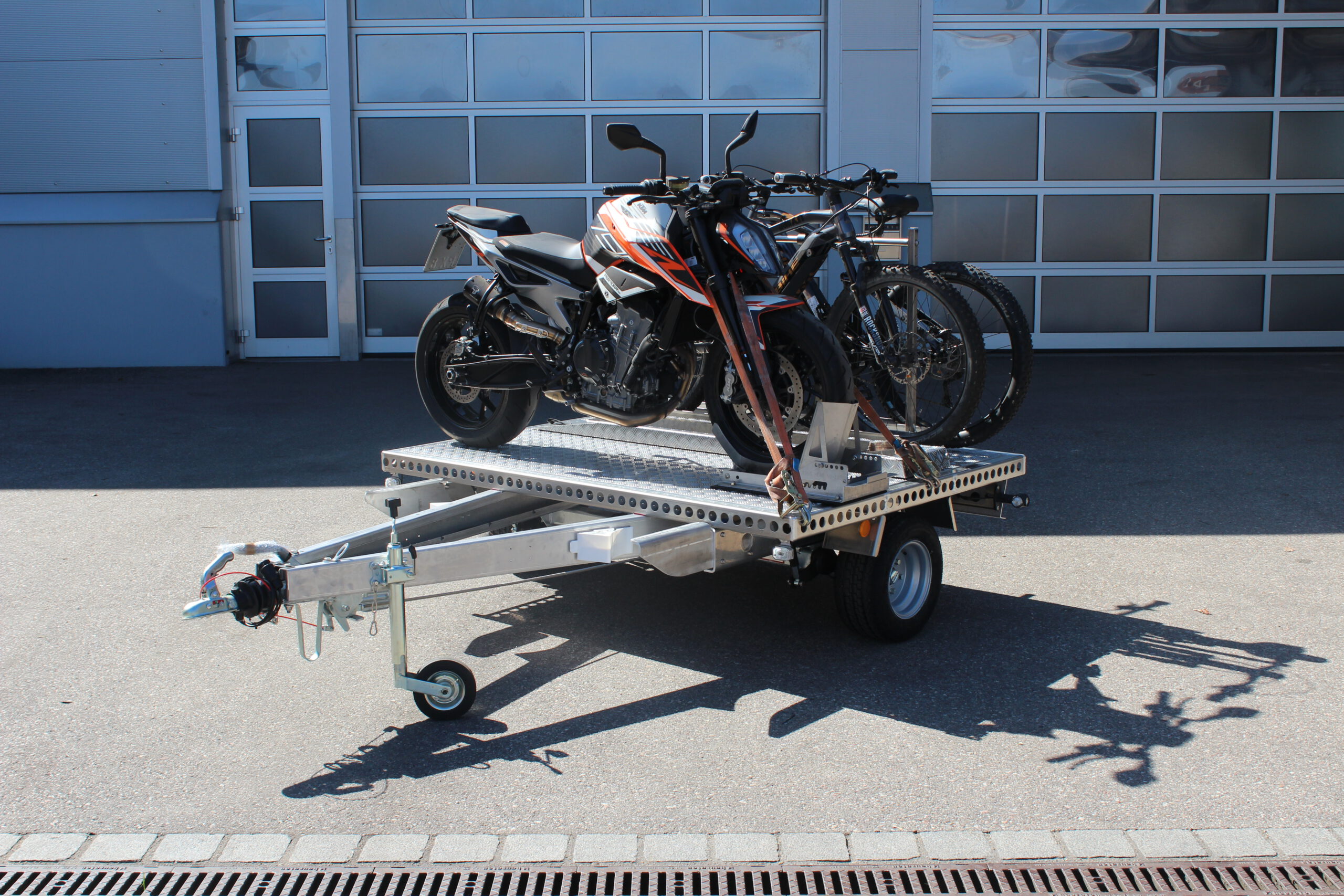UA150 Quer Anhänger mit einer KTM Duke und zwei Fahrrädern beladen vor einer Halle