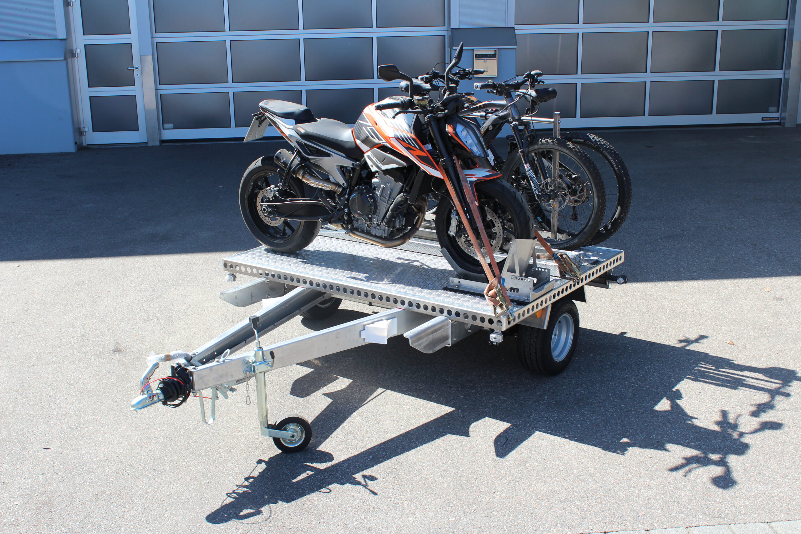 UA150 Quer Anhänger mit einer KTM Duke und zwei Fahrrädern beladen vor einer Halle