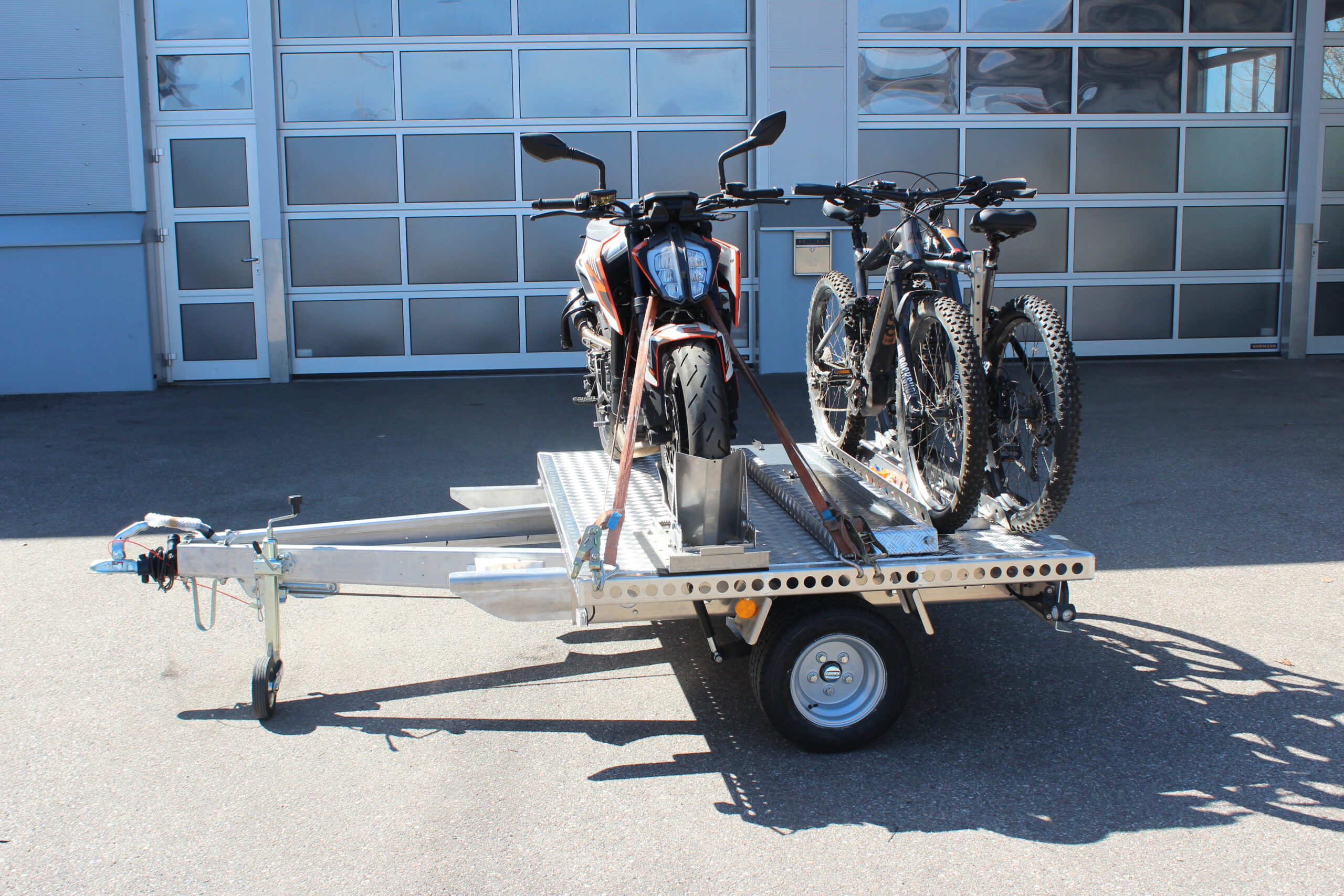 UA150 Quer Anhänger mit einer KTM Duke und zwei Fahrrädern beladen vor einer Halle